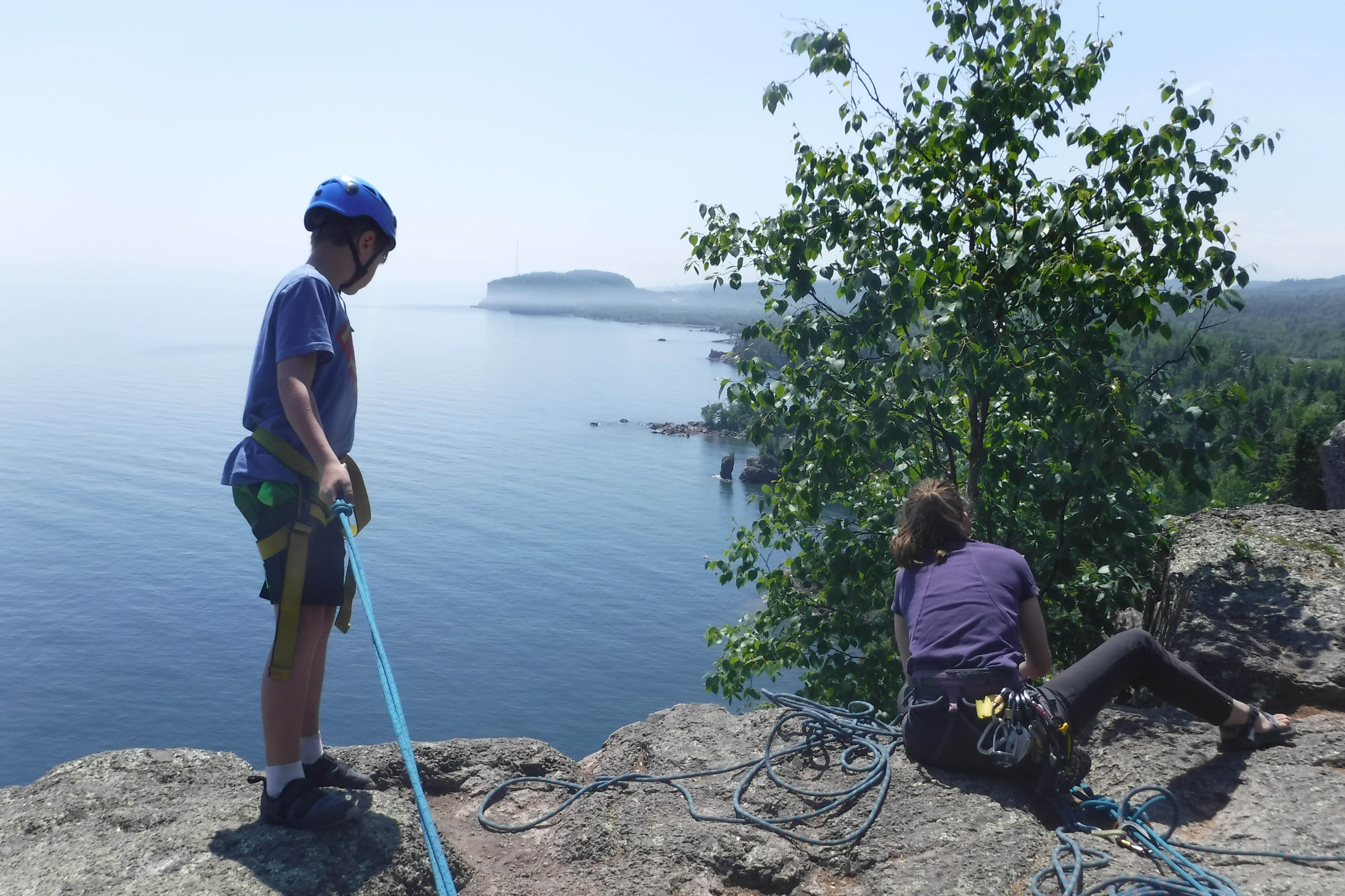 A boy and girl on a rock cliff overlooking water
