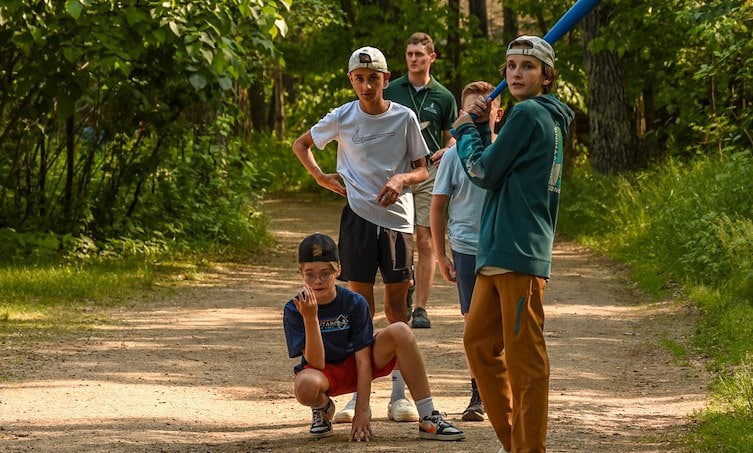 A group of boys on a dirt path with a baseball bat