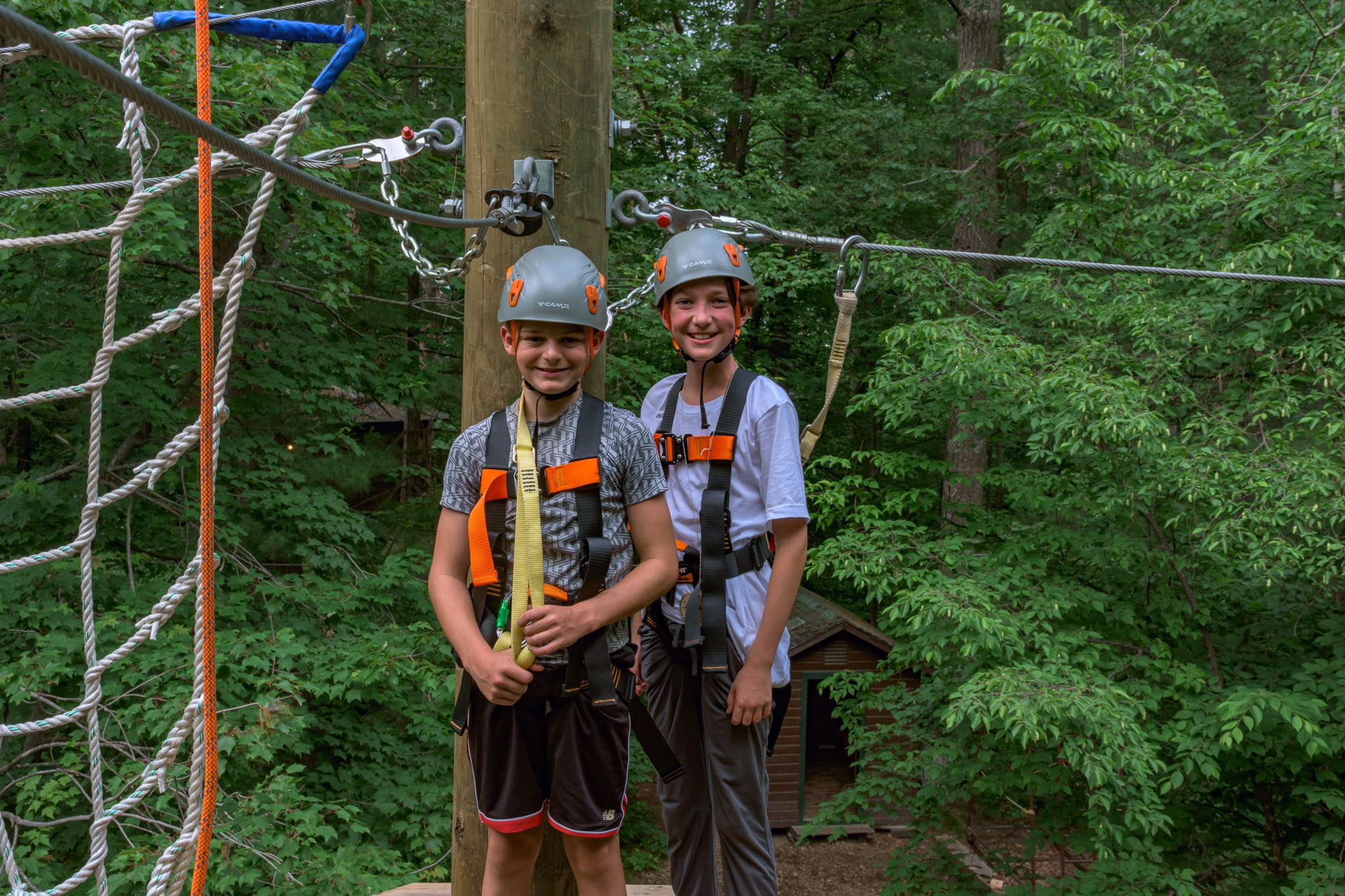 Two boys wearing safety harnesses and standing in a rope park