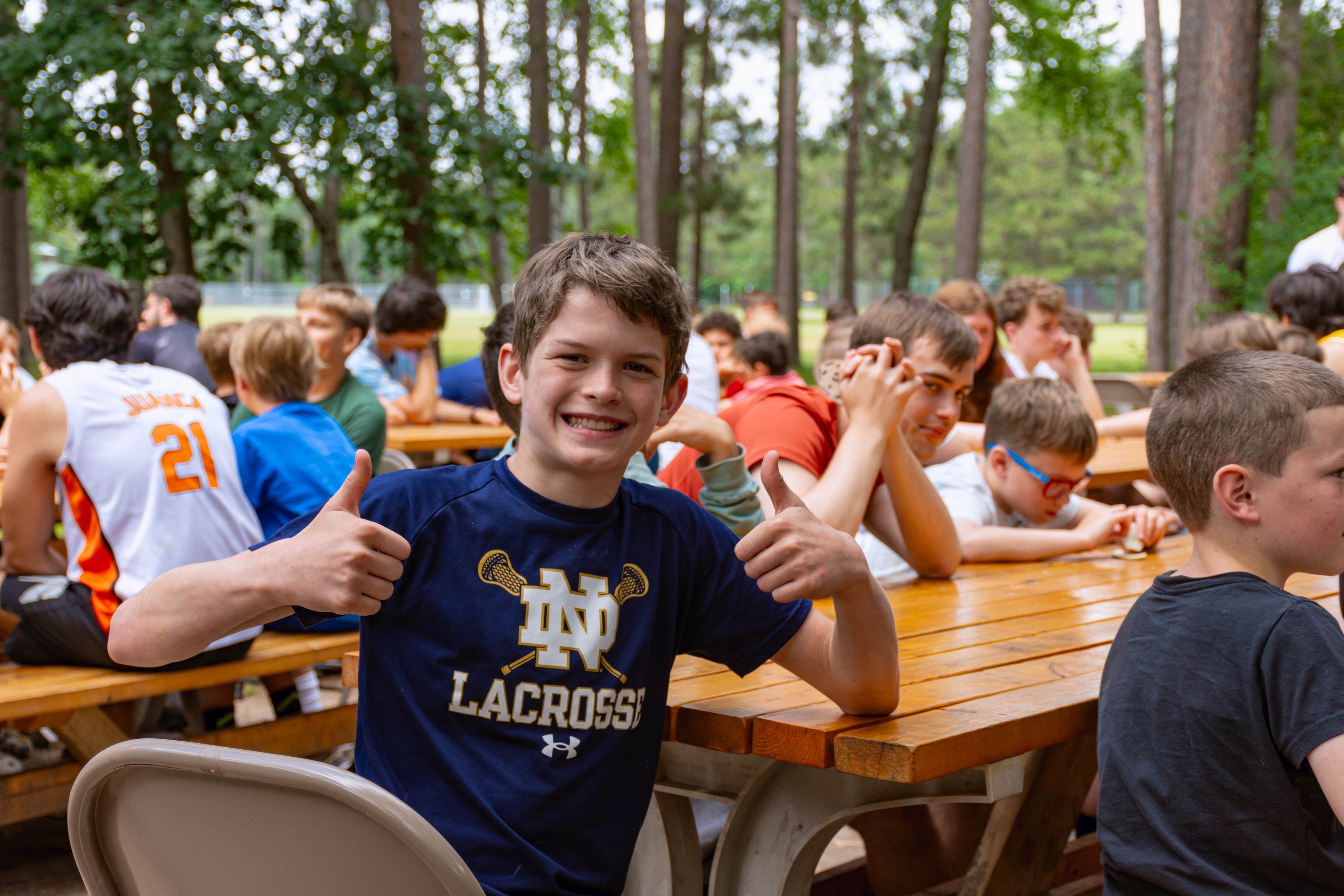 A boy giving a thumbs up with other people sitting at a picnic table
