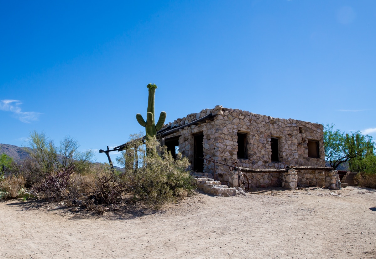 A stone building in the desert with a cactus and mountain view