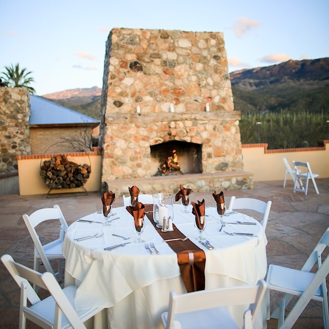 A round table set for dinner with a stone fireplace in the background on an outdoor patio.