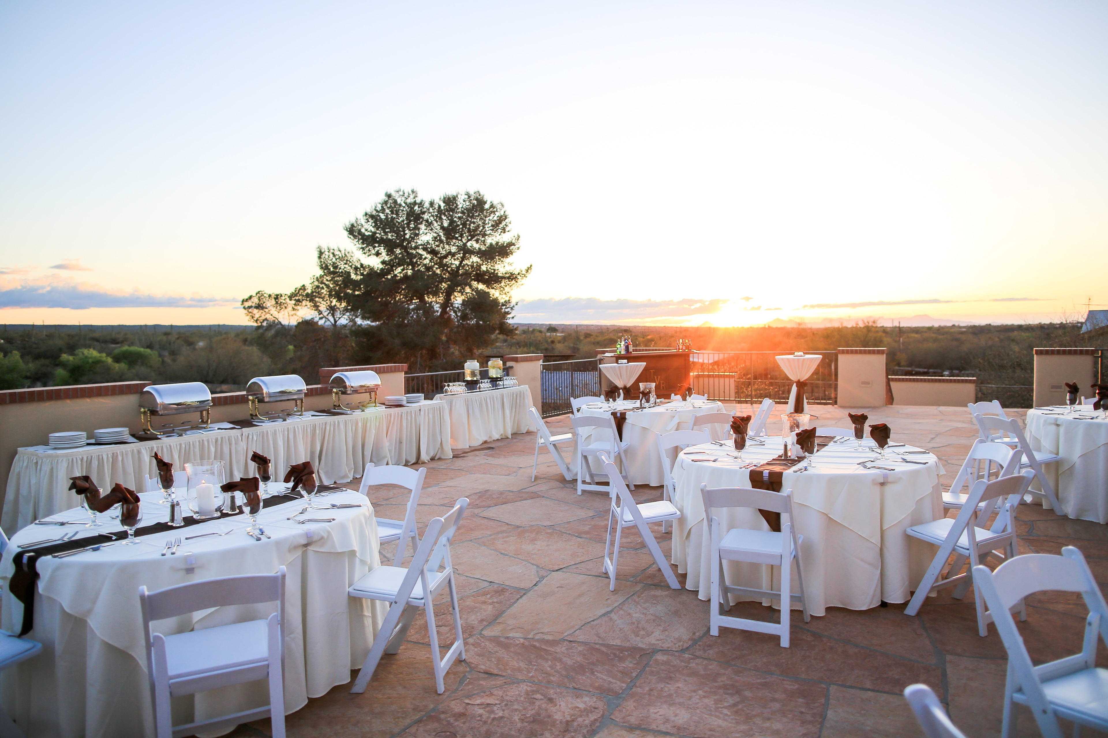 An outdoor patio with white tables and chairs set for an event at sunset.