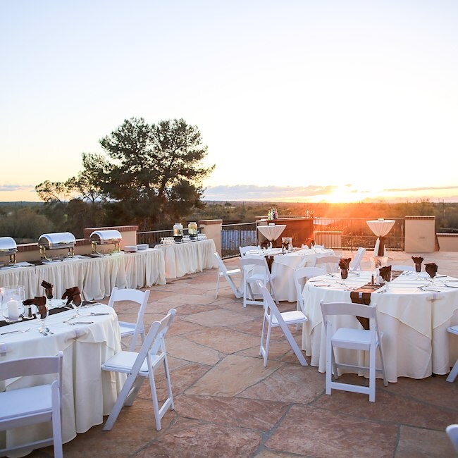 An outdoor patio with white tables and chairs set for an event at sunset.
