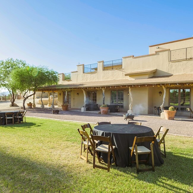 A large, tan-colored building with a patio area and outdoor tables and chairs.