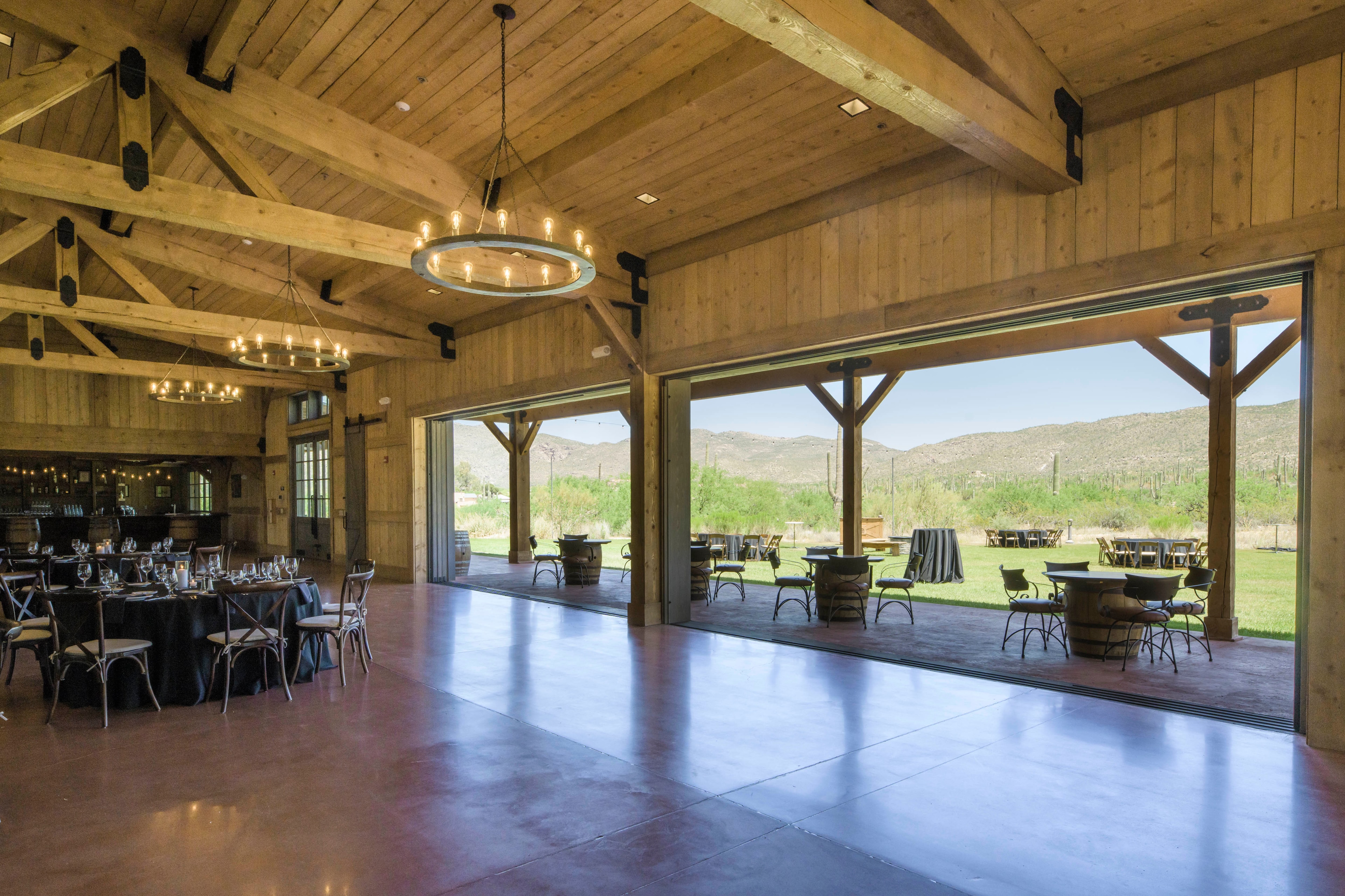 A large dining area with wooden beams, large windows, and outdoor seating.