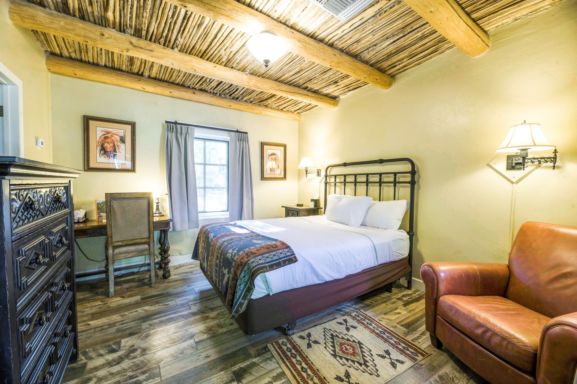 A wide-angle view of a rustic guest room with a king-size bed, leather armchair, and wooden desk.