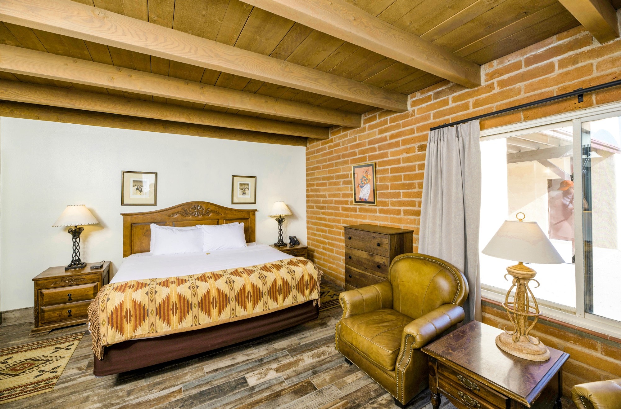 A wide view of a rustic guest room with a large bed, wooden furniture, and a brick accent wall.