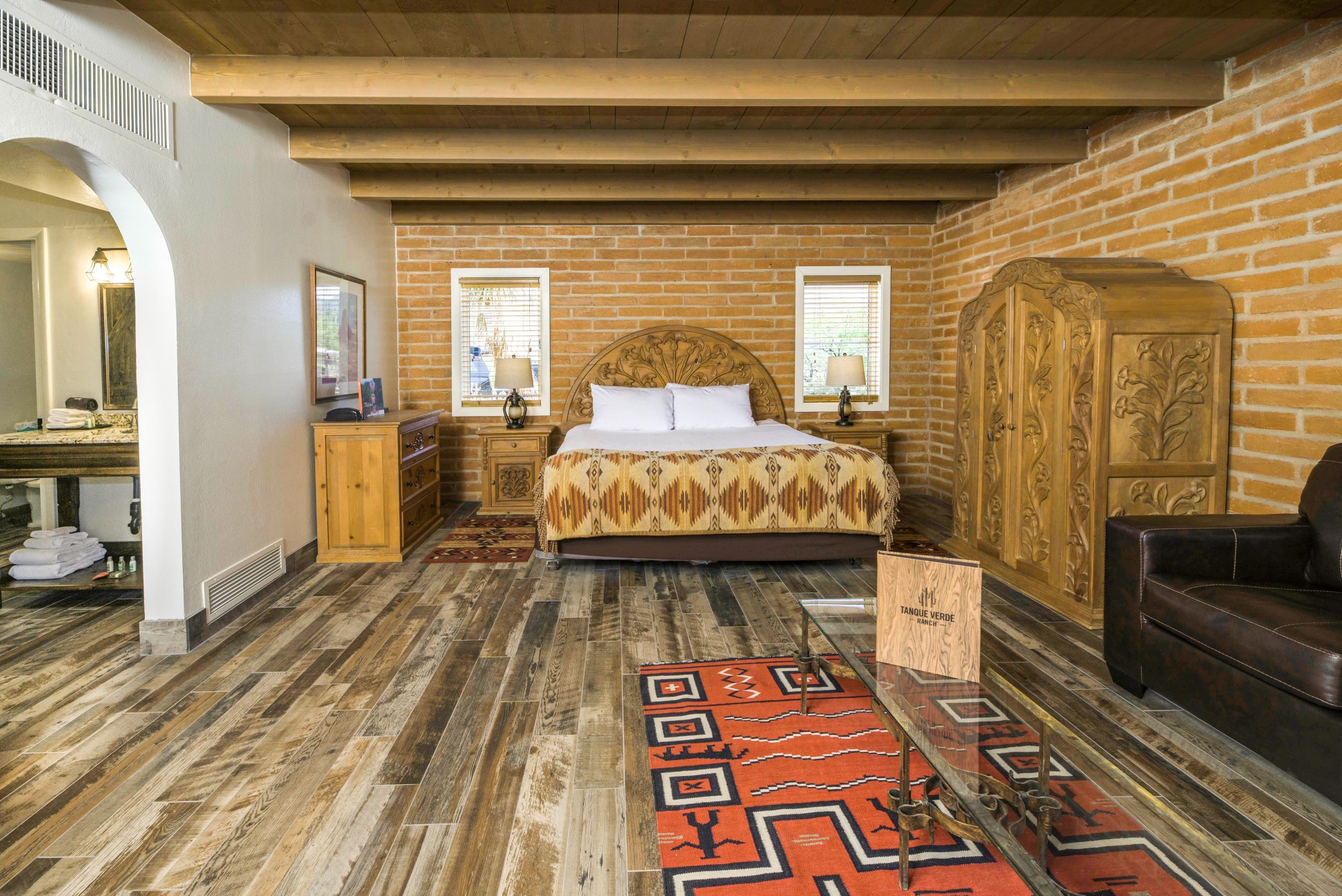 A wide view of a guest room with a large bed, wooden furniture, and a colorful rug.