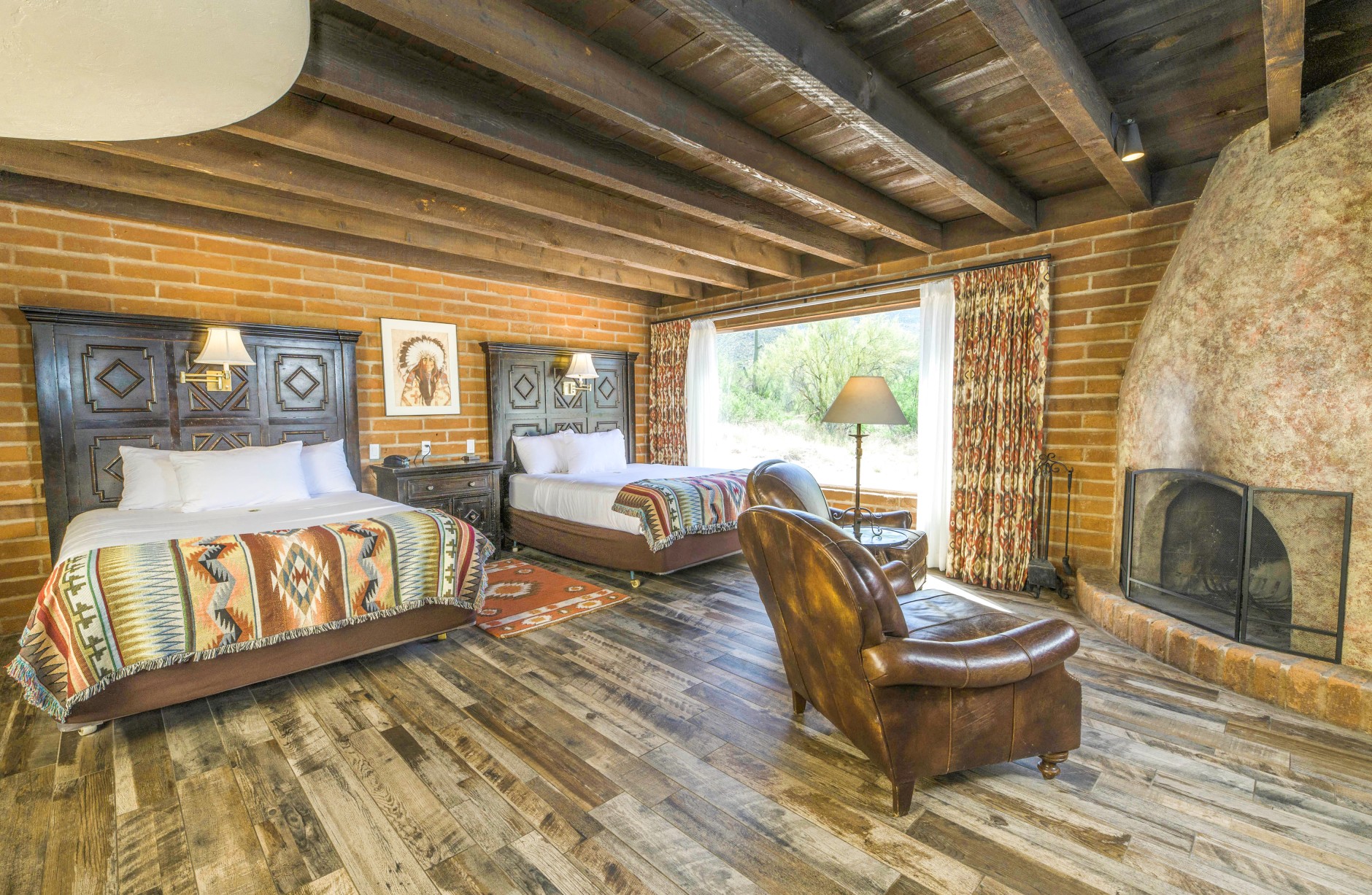 A wide view of a rustic hotel room with two beds, a fireplace, and a leather armchair.