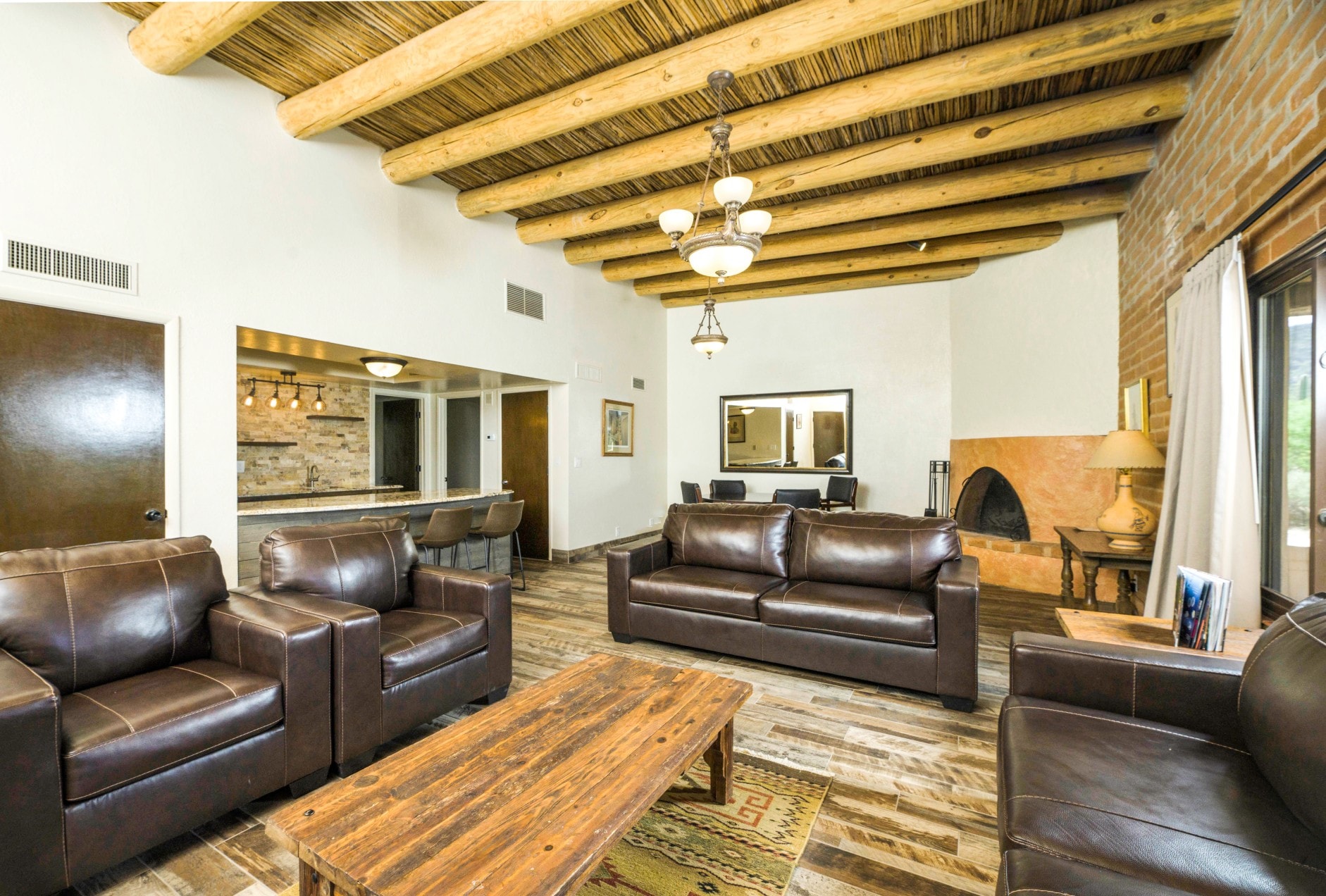 A large lobby with a high ceiling, wooden beams, leather furniture, a fireplace, and a kitchenette.