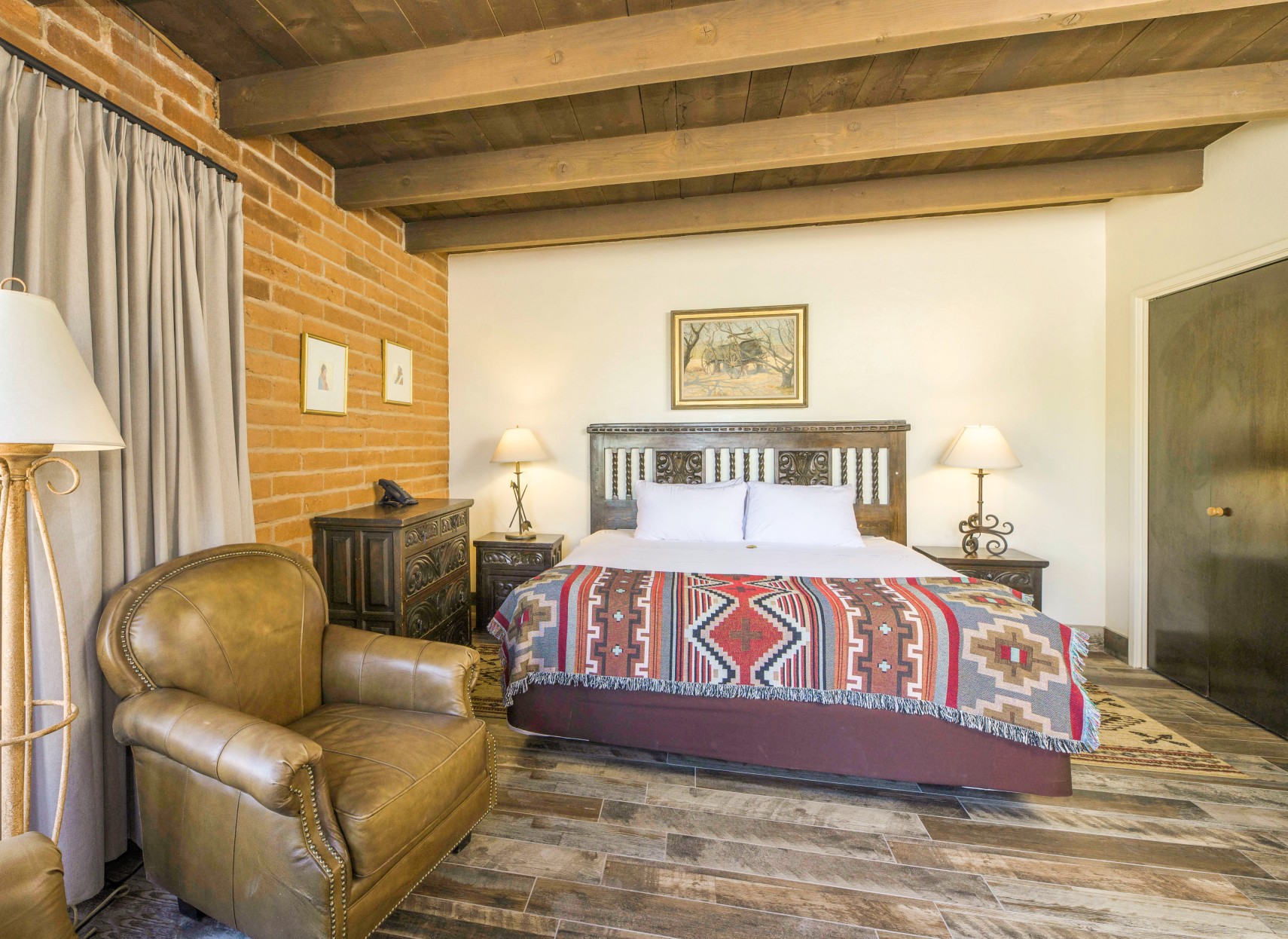 A wide view of a guest room with a bed, leather armchair, and exposed beams.