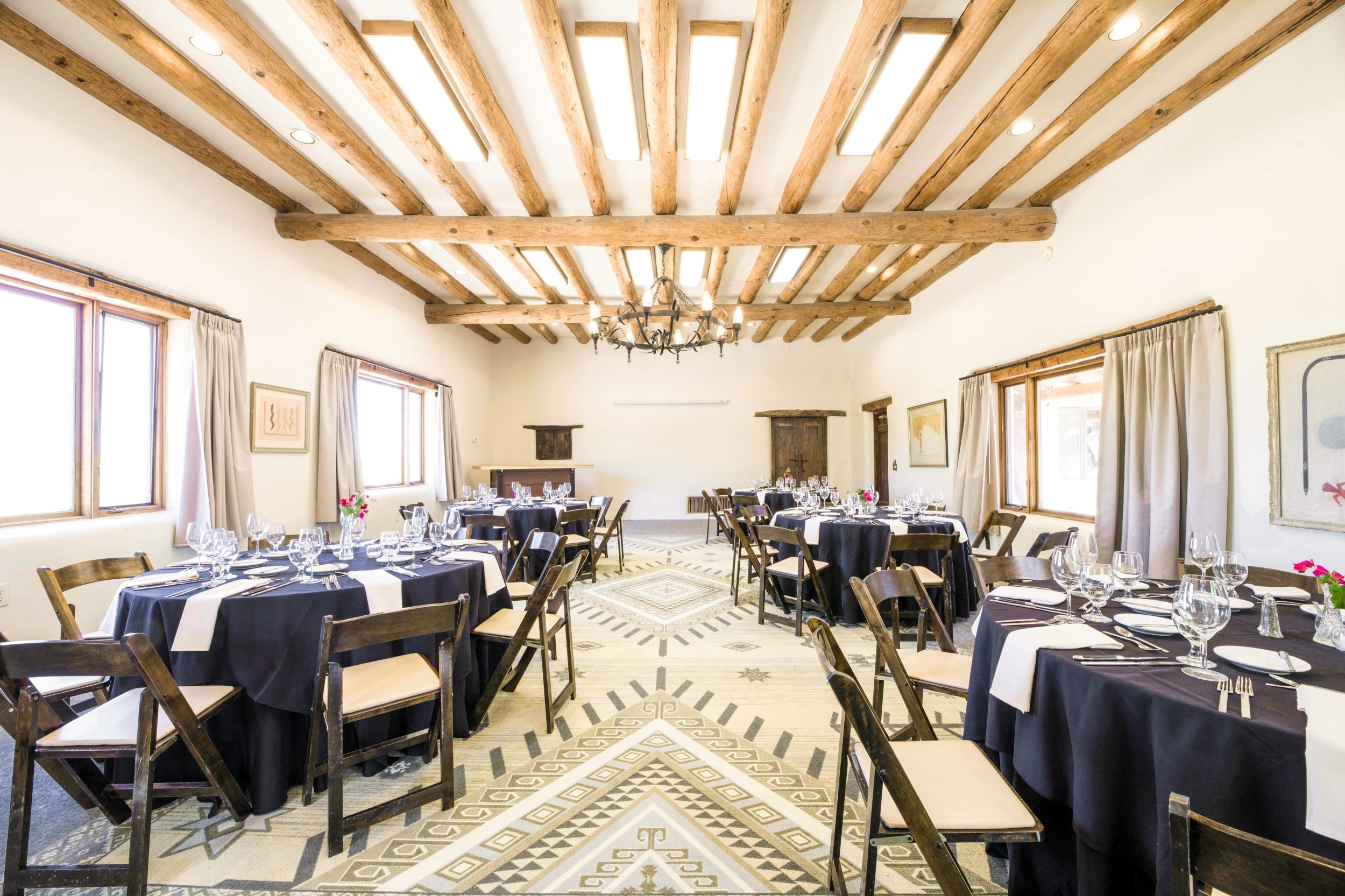 A large dining room with a high ceiling, wooden beams, and a chandelier, set with multiple tables for dining.