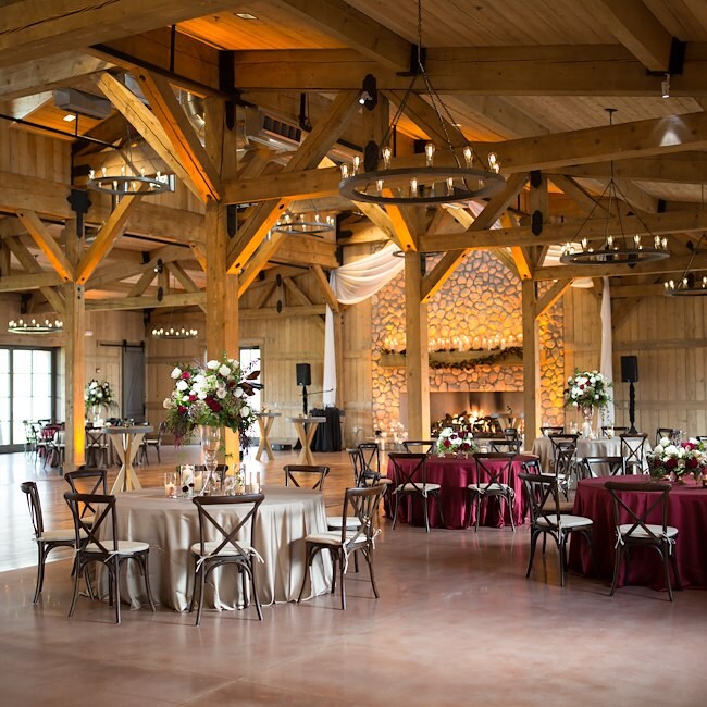 A large indoor event space with wooden beams, tables, chairs, and floral arrangements.
