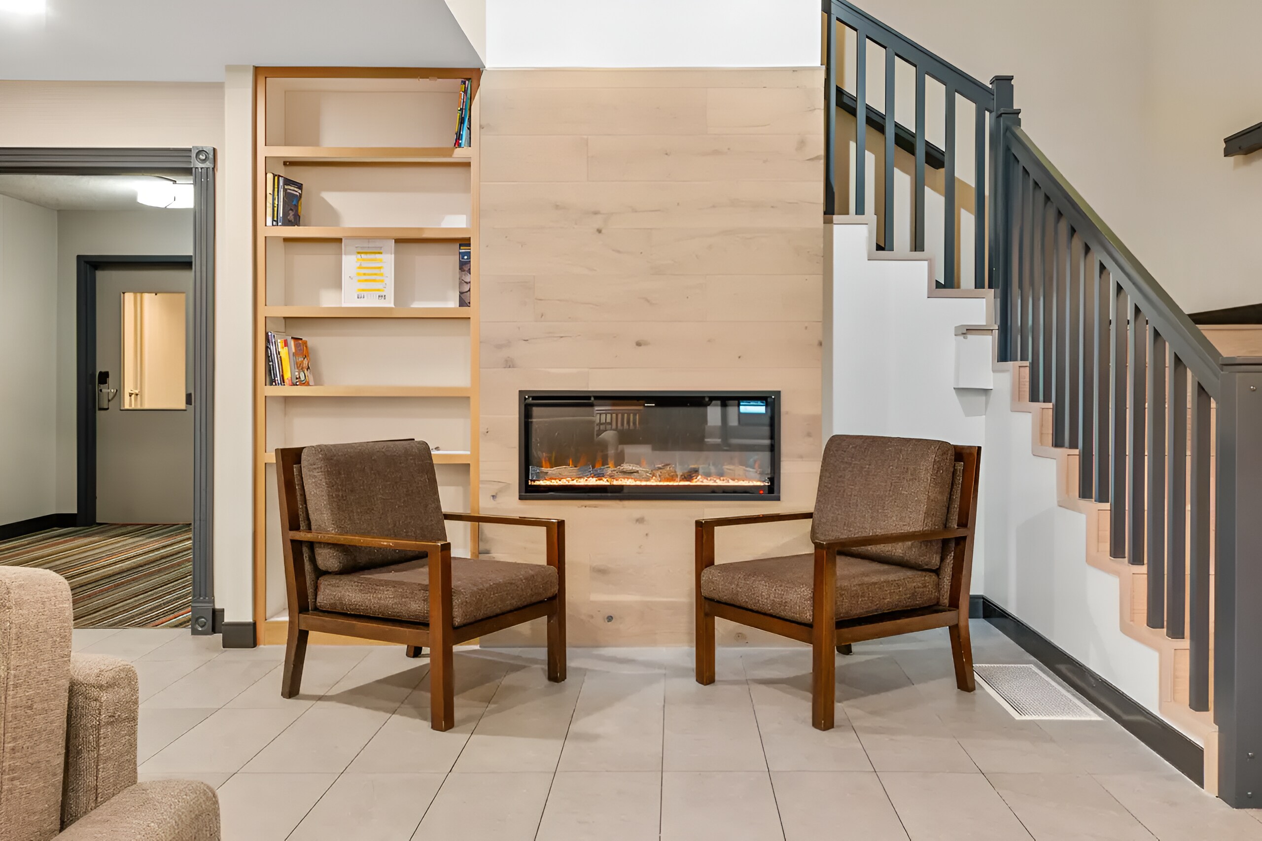 Cozy seating area with two brown armchairs facing an electric fireplace set in a light wood panel