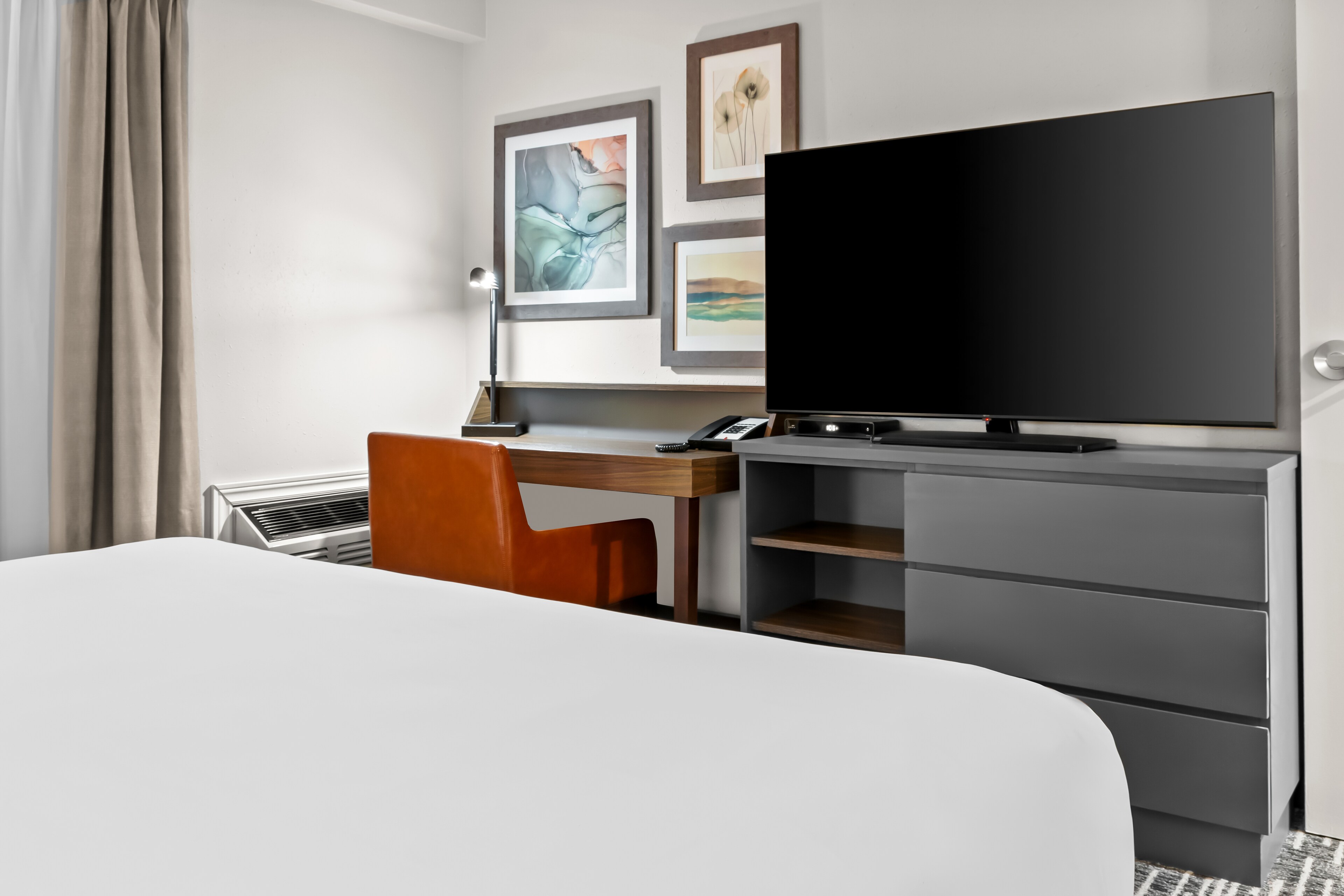 Modern hotel room with a large bed, a sleek desk, an orange chair