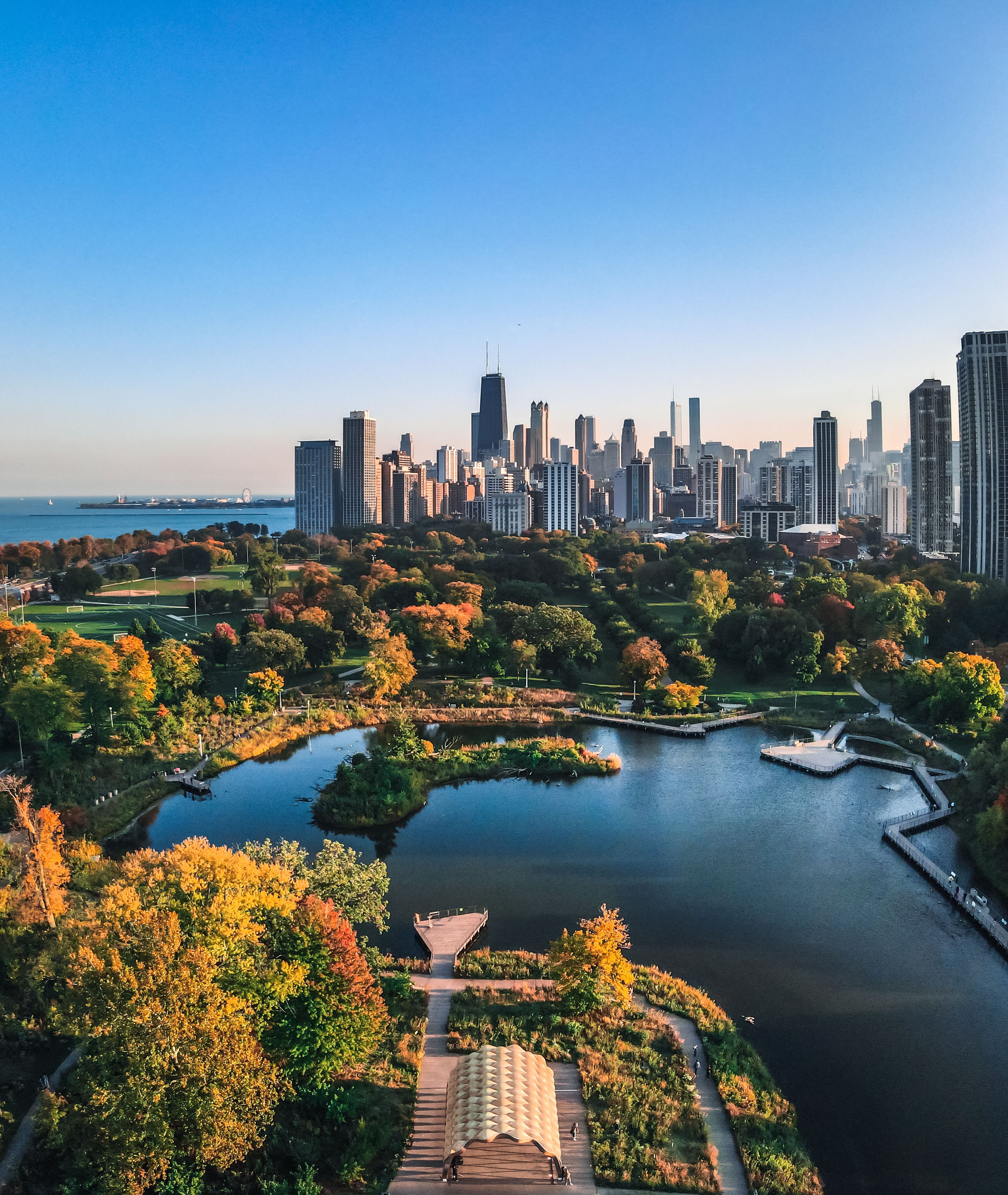 Aerial view of Chicago’s skyline beyond a tree-lined park and reflective lagoon