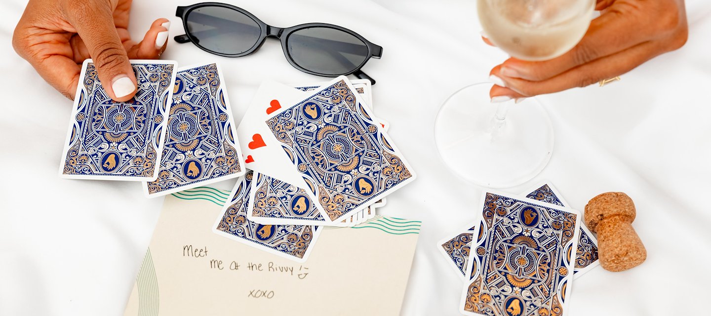 Top-down view of hands playing cards beside sunglasses, champagne, corks