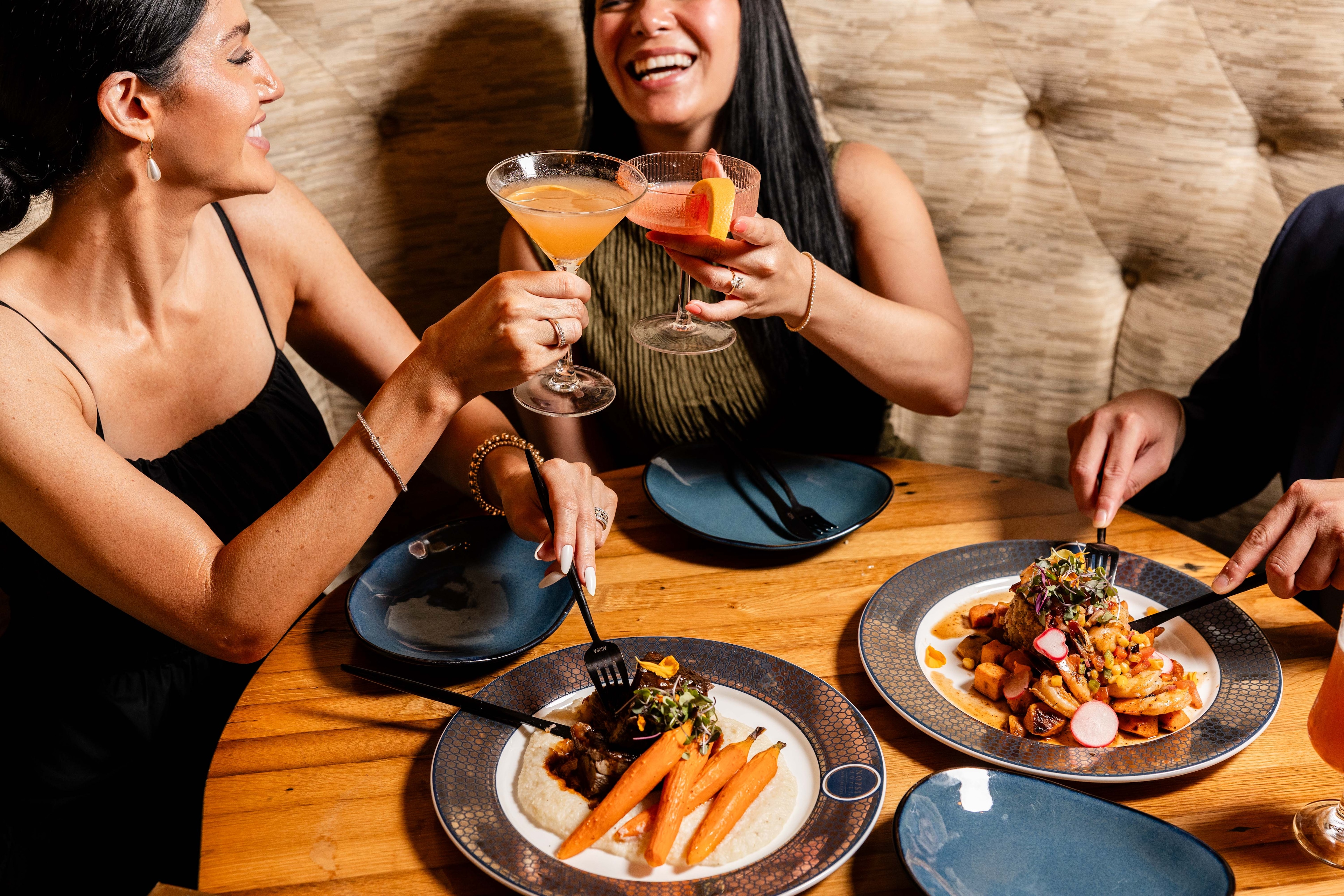A dinner table with food and drinks, and two people clinking glasses