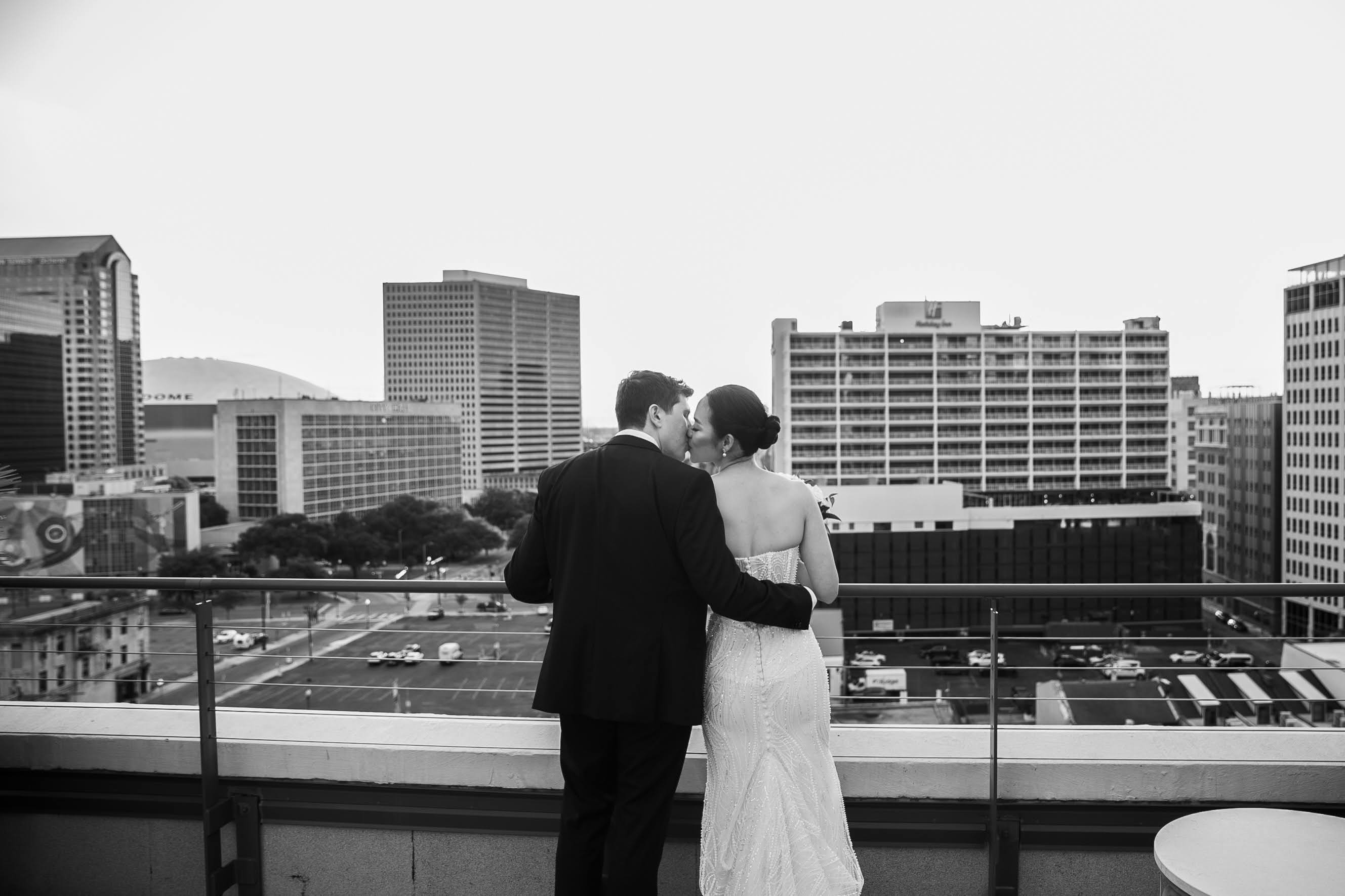 A black and white photo of a couple standing on a rooftop with a city view.