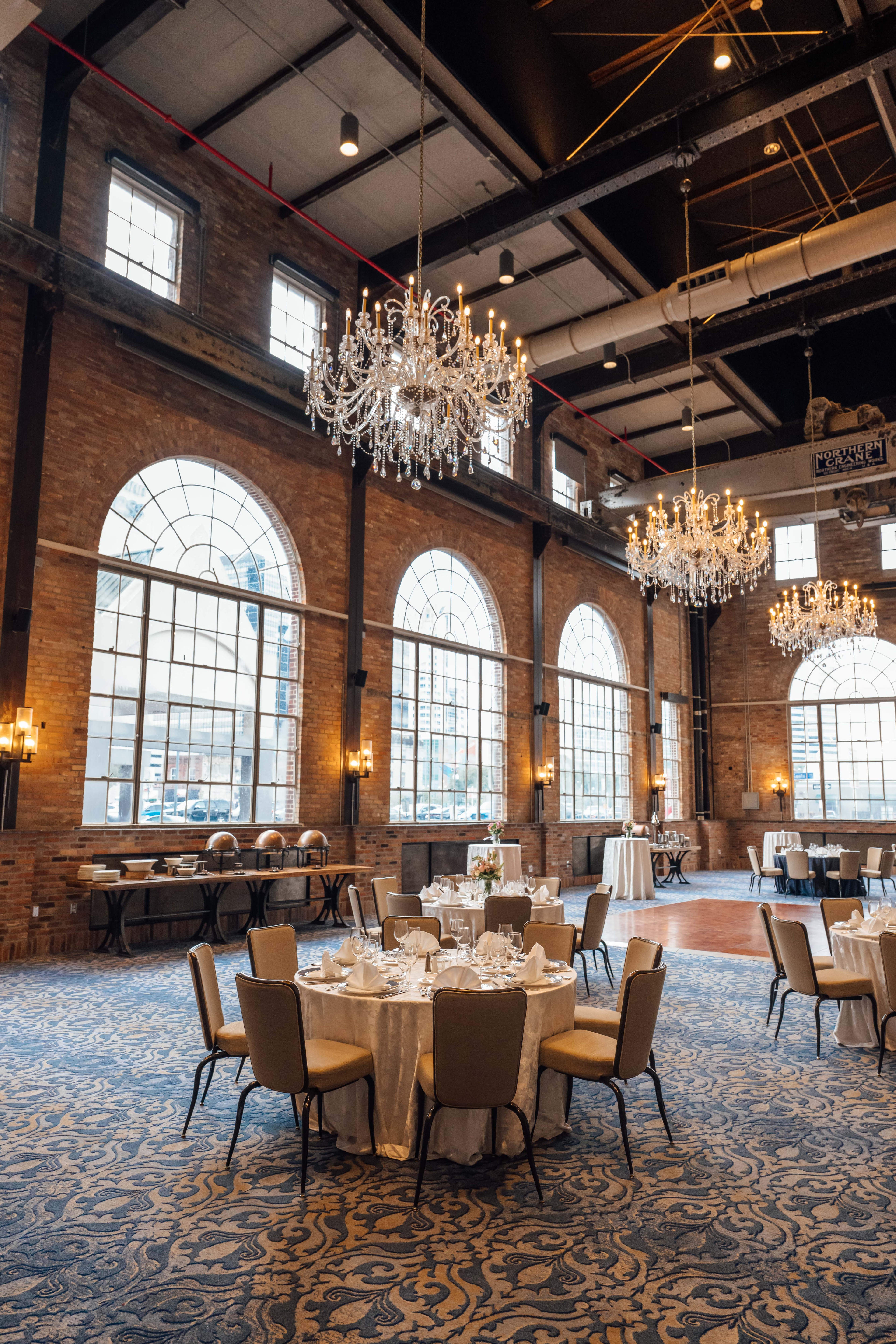 A large, elegantly decorated meeting room with round tables, white linens, and chandeliers.
