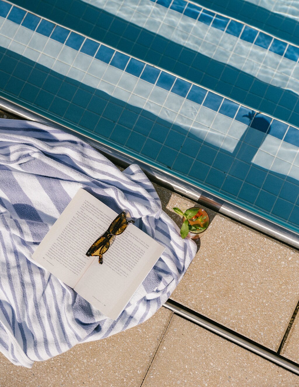 A relaxing poolside scene with a striped towel, an open book, and sunglasses