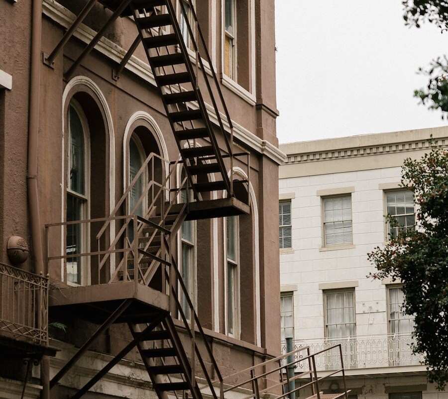 Facade of a brown brick building with arched windows and a metal fire escape