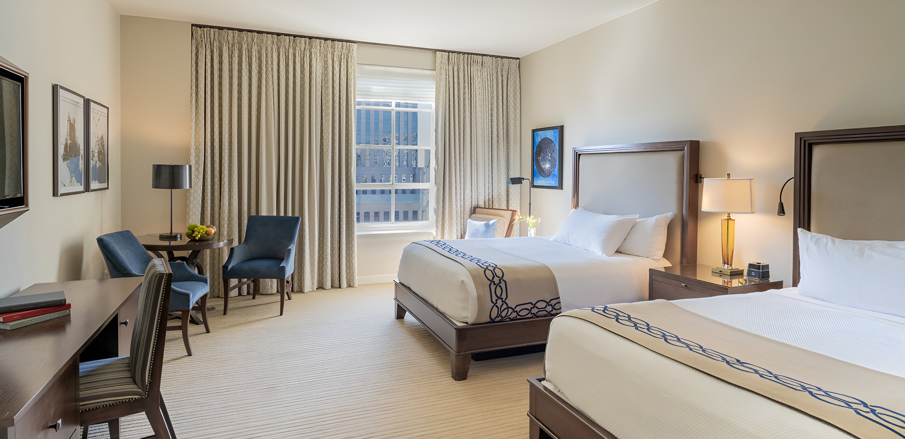 A wide view of a hotel room with two queen beds, a window with city view, and a desk area.