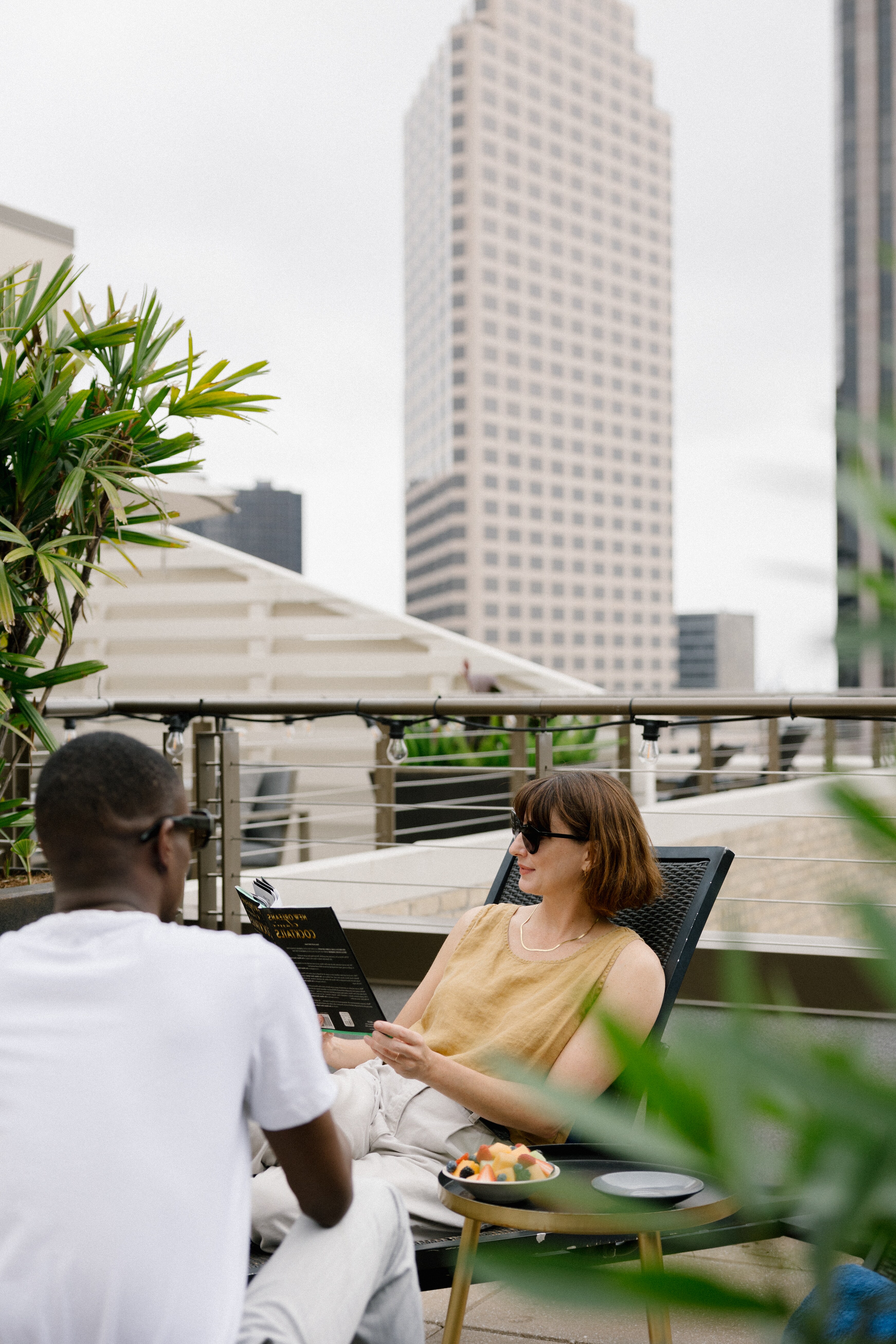Two people relax on a rooftop patio with city buildings in the background