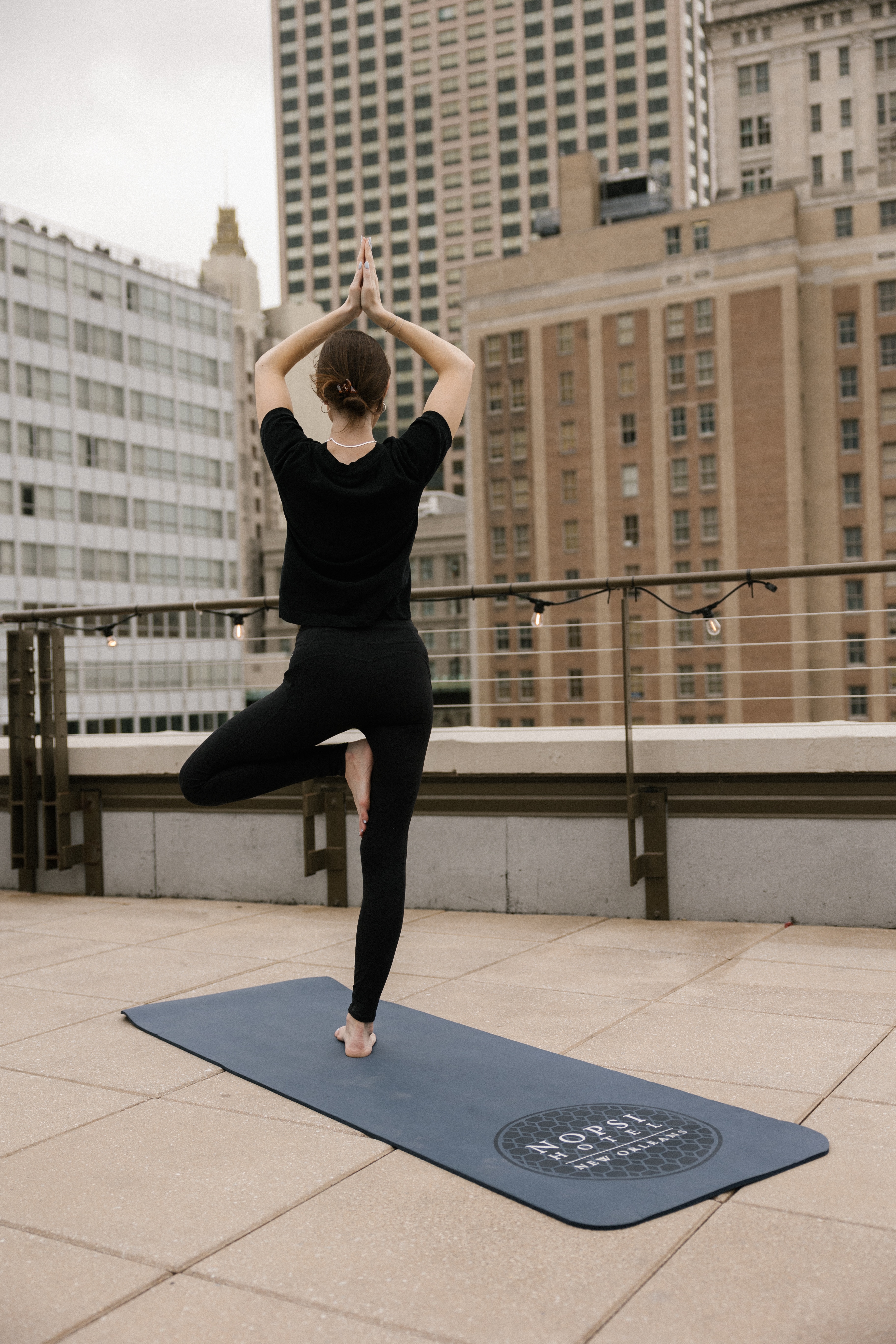 A woman practices yoga on a rooftop with a city skyline view.