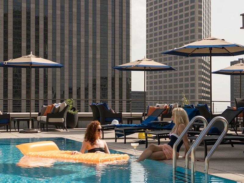 Two women relax by the rooftop pool with a city skyline view.