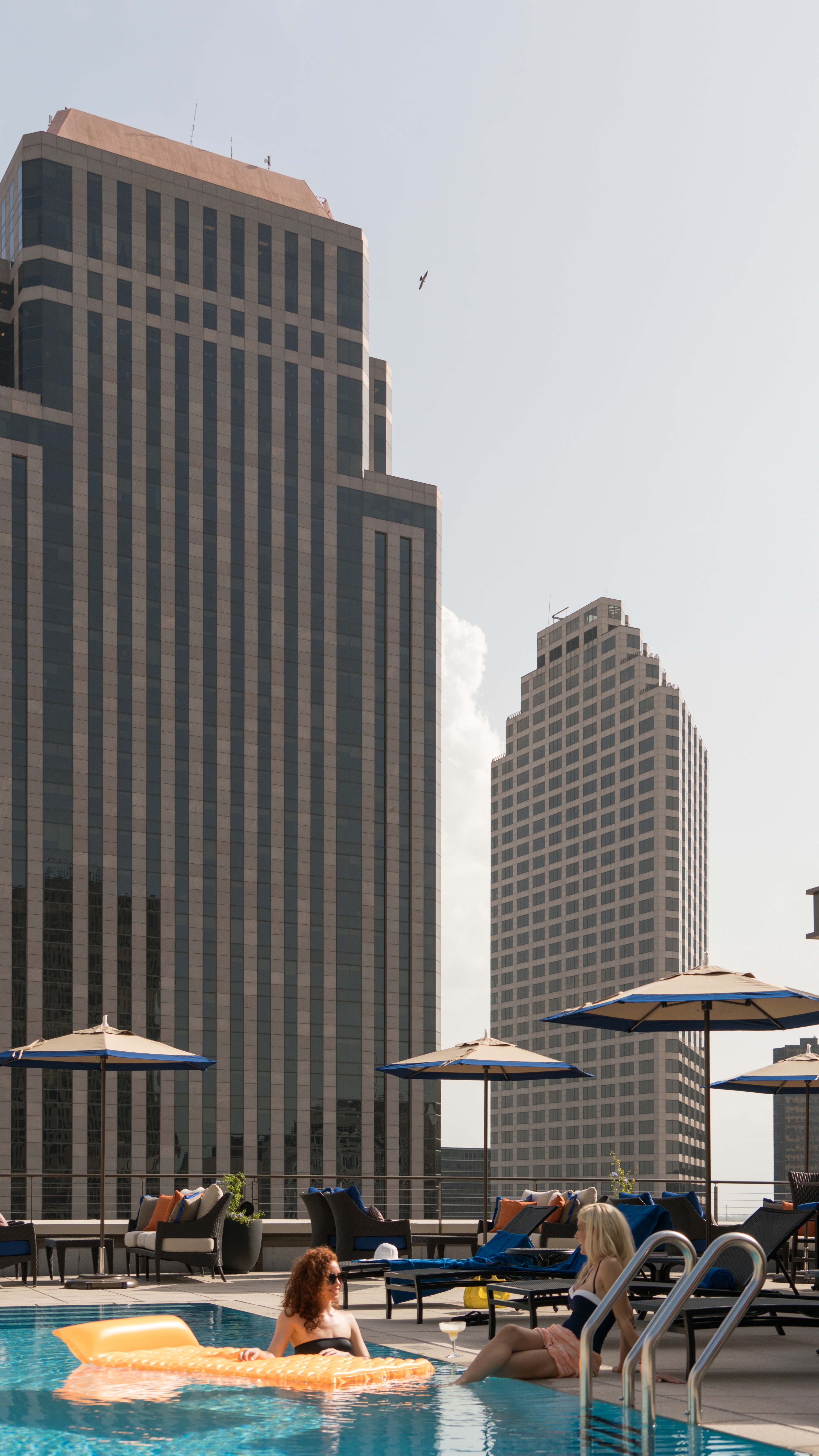 Two women relax by the rooftop pool with a city skyline view.