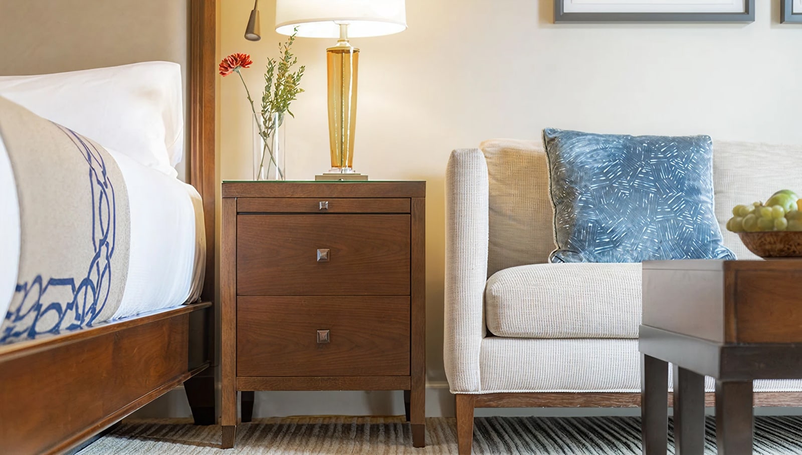 A neatly arranged hotel room with a wooden bed, nightstand, lamp, and chair.