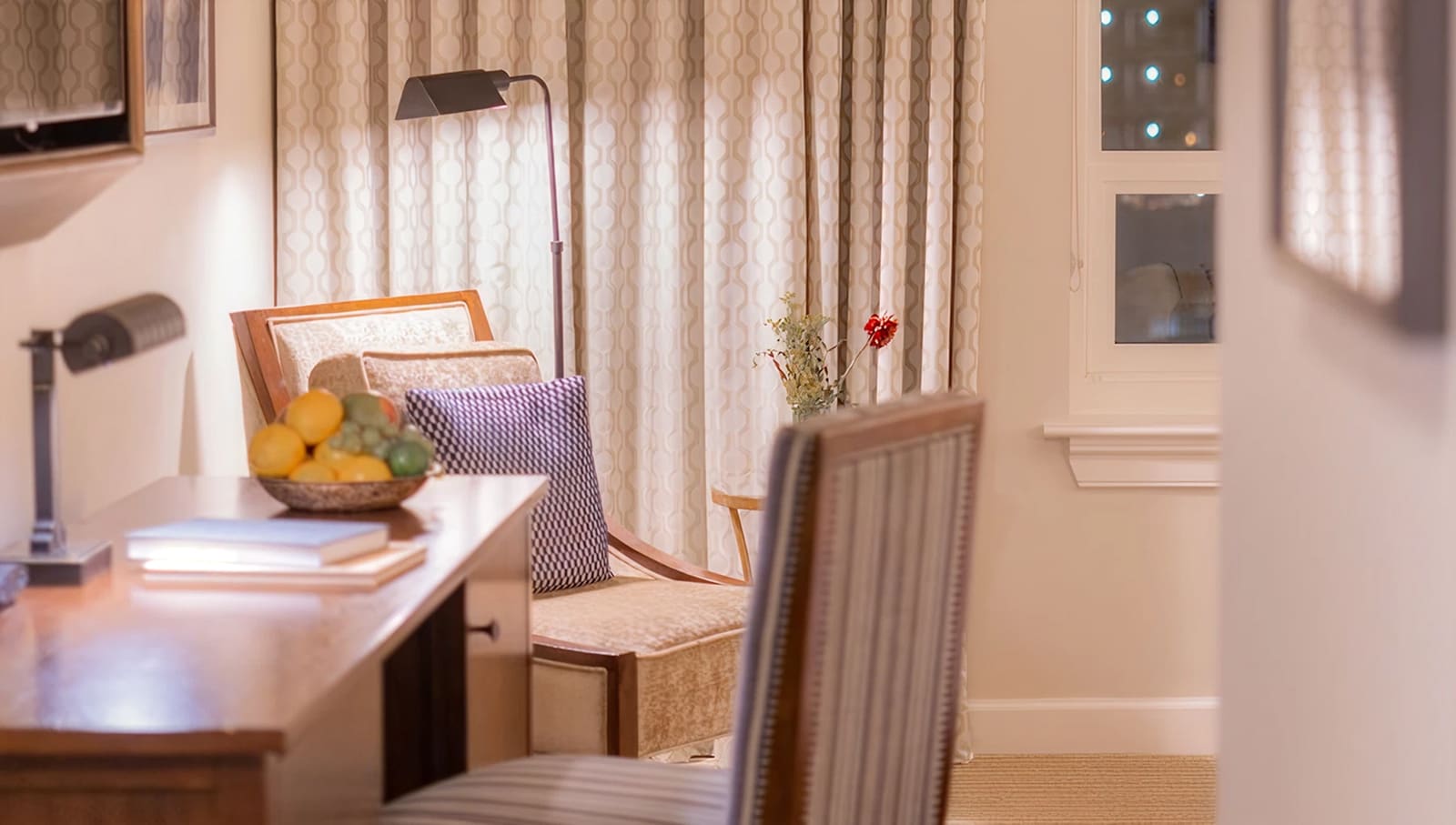 A well-lit guest room with a desk, chair, and fruit bowl.