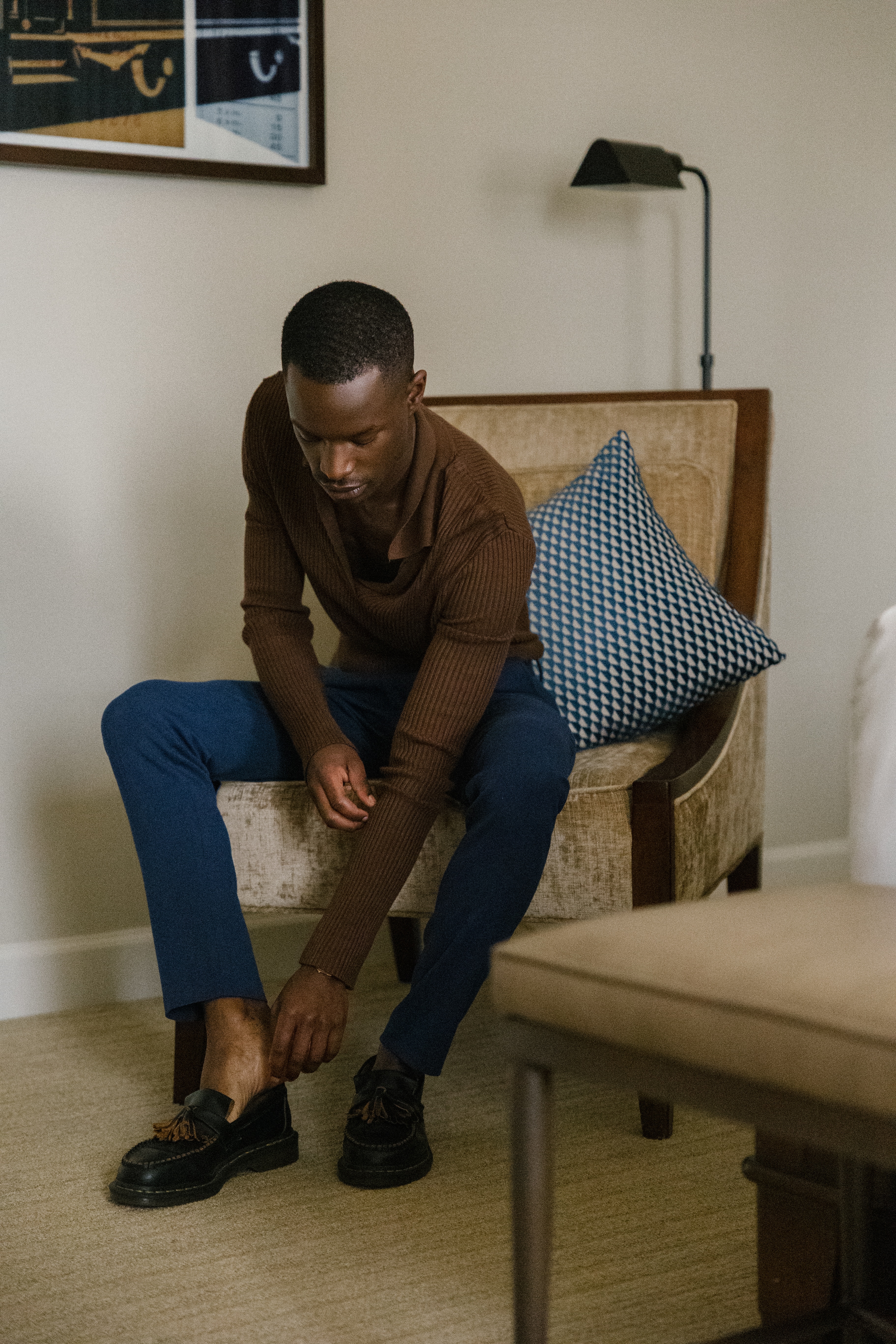 A man sitting in a chair tying his shoes in a room with beige walls and carpet.
