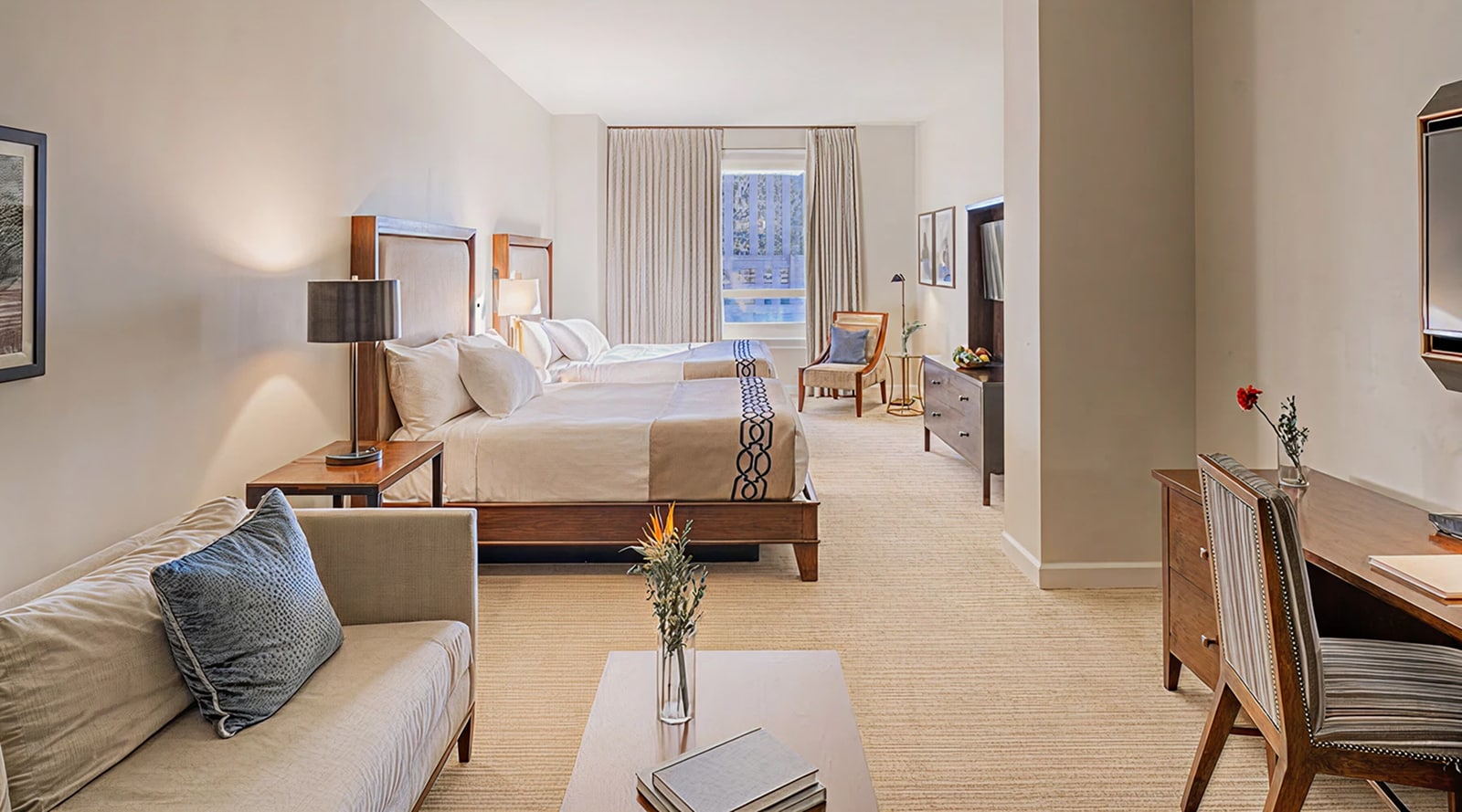A wide view of a hotel room with a bed, sofa, desk, and TV.