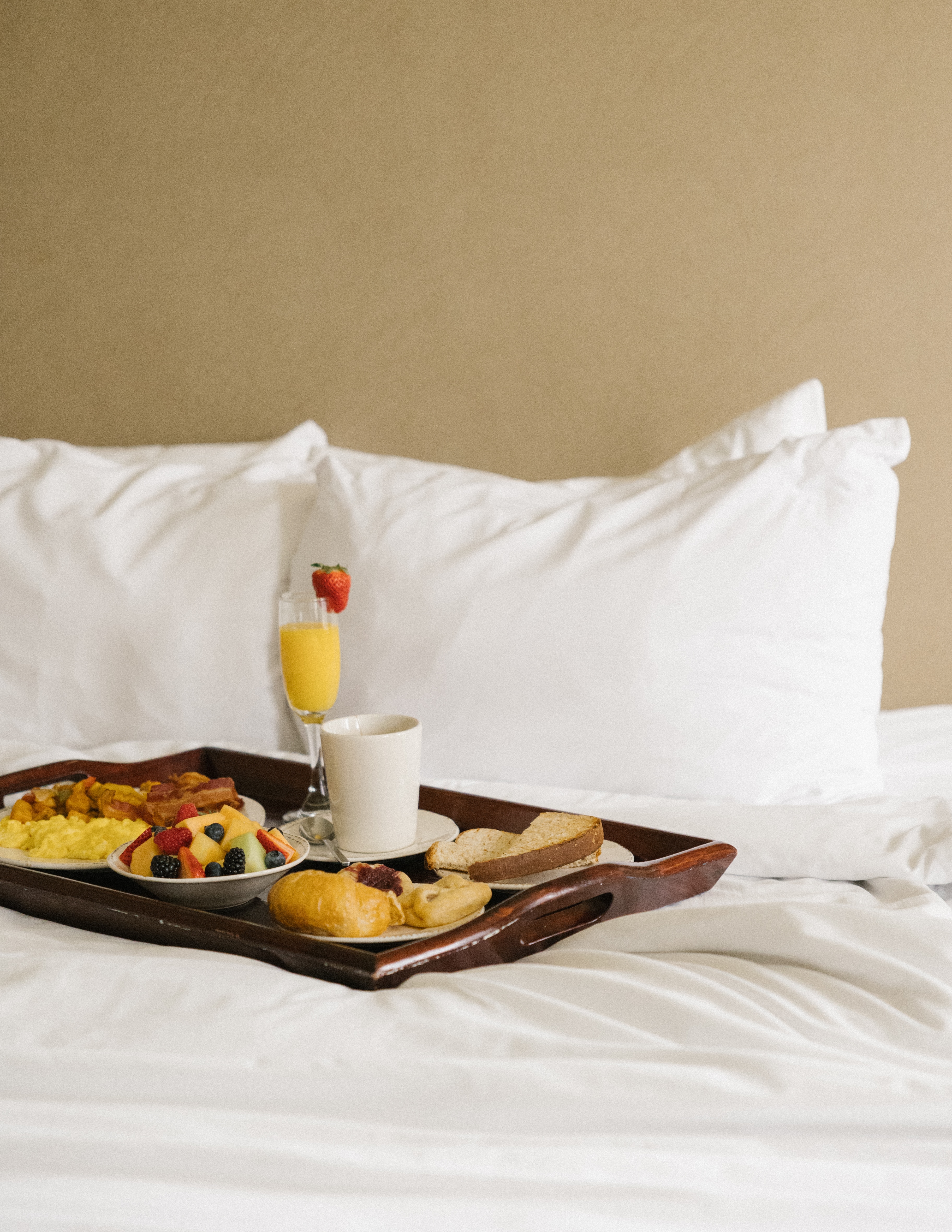 A breakfast tray on a bed with white linens and pillows