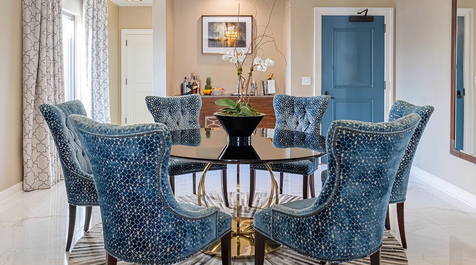 A dining area with a round glass table and six blue upholstered chairs.