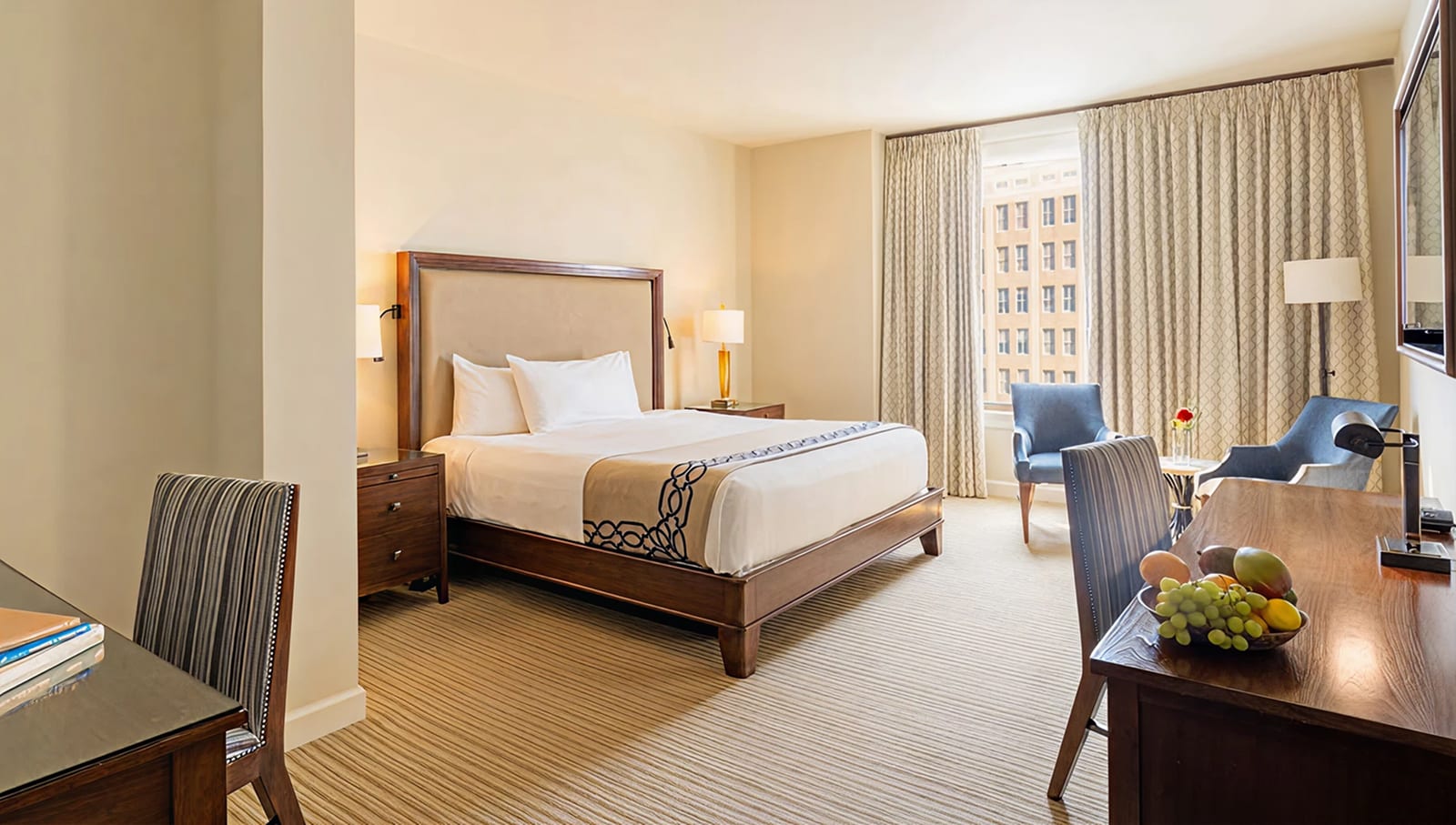 A wide view of a hotel room with a bed, desk, chair, and window.
