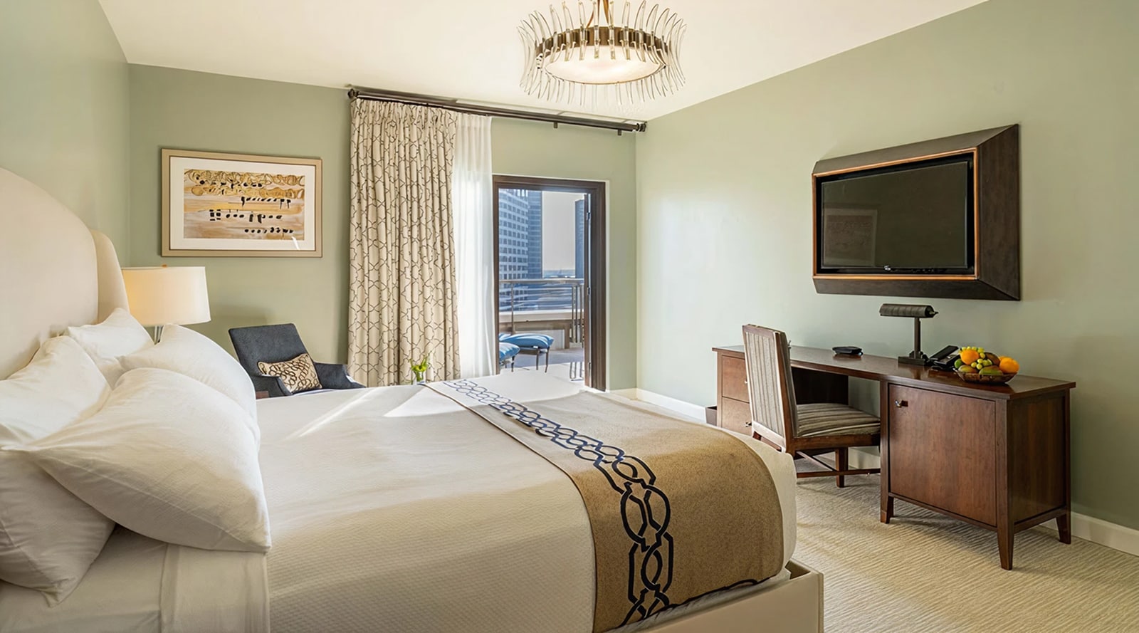 A wide view of a hotel room with a bed, desk, TV, and balcony door.