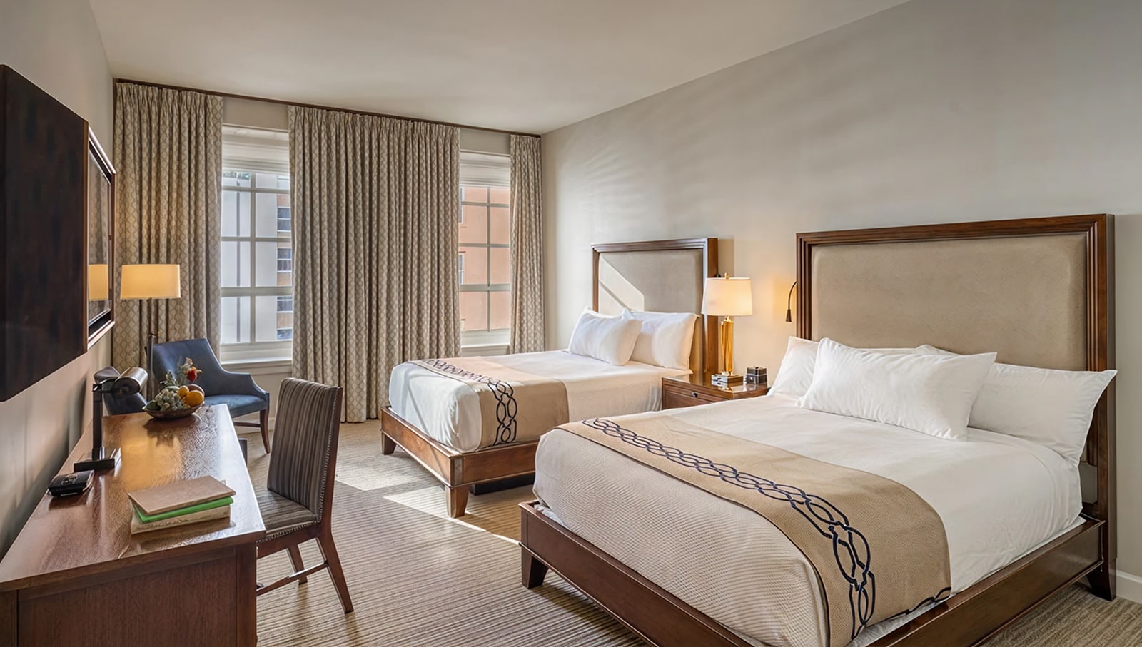 A hotel room with two beds, a desk, and a window.