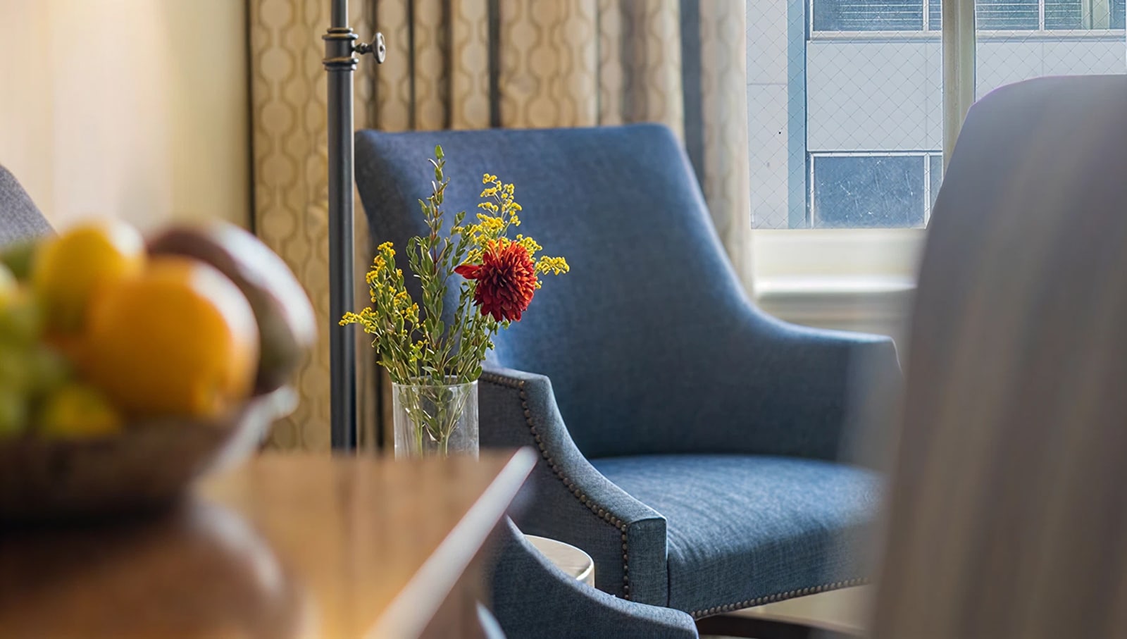 A blue armchair with a vase of flowers on a wooden table in a hotel room.