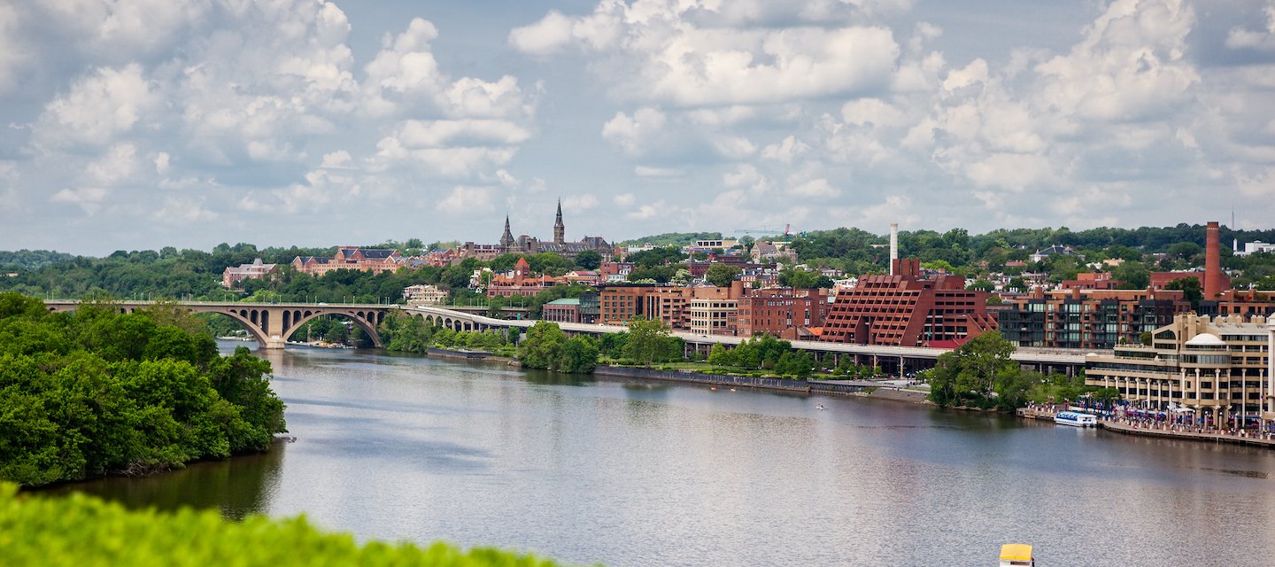 Scenic view of a river with a boat, surrounded by green trees and a cityscape