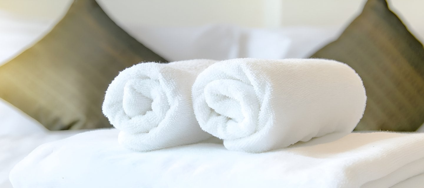 Fresh white rolled towels on a neatly made bed, representing the welcoming services and amenities at The Inn at Virginia Tech