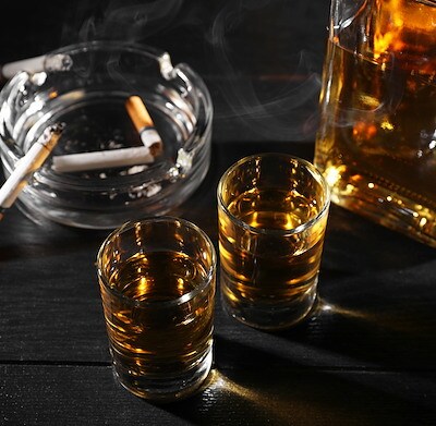 Alcohol addiction. Whiskey in glasses, smoldering cigarette and ashtray on black wooden table