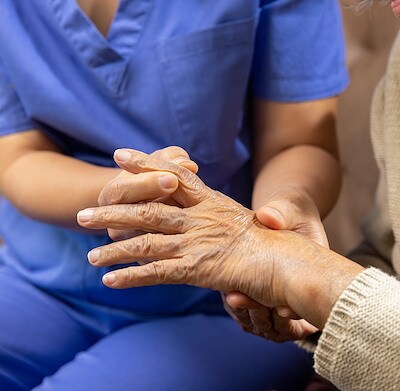 Caregiver massaging finger of elderly woman in painful swollen gout.