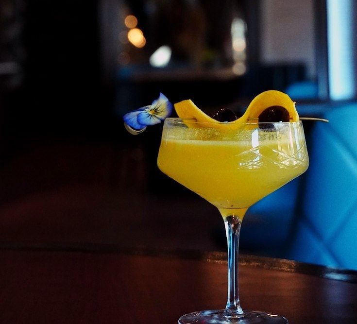 Cocktail garnished with a flower, cherry, and lemon served at The Henley Southlake