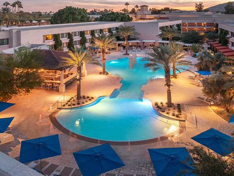 A pool with palm trees and umbrellas in front of a building