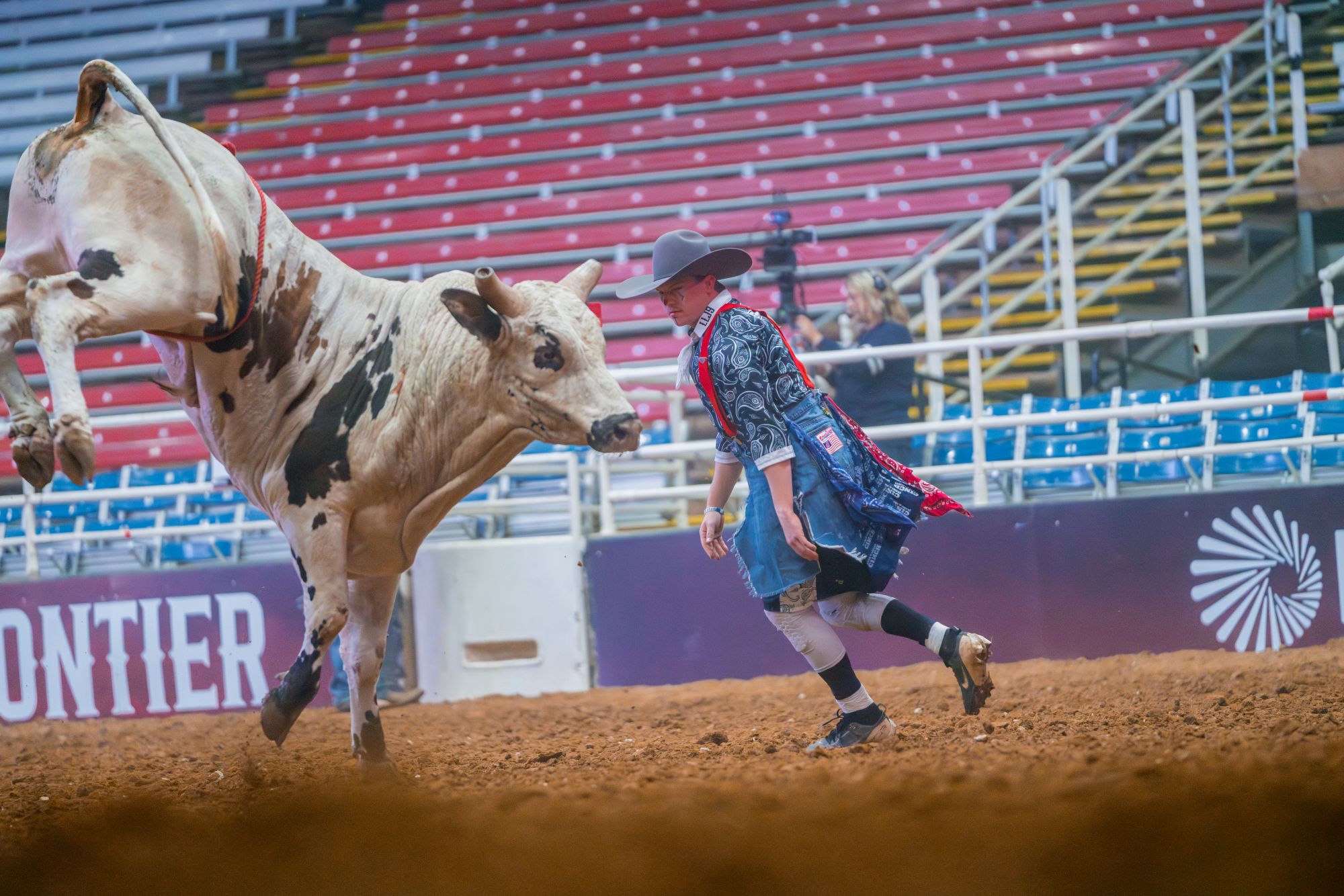 A man in a cowboy hat running with a cow in a arena