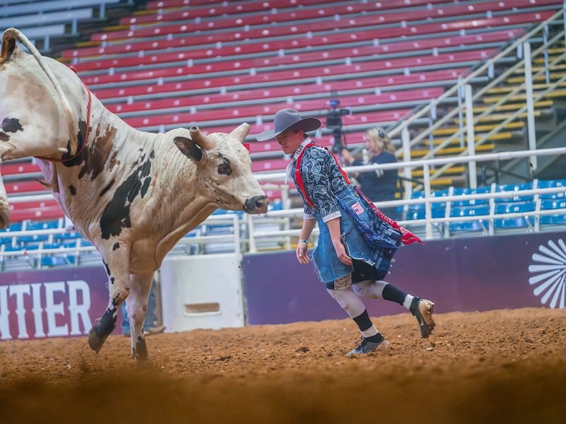 A man in a cowboy hat running with a cow in a arena